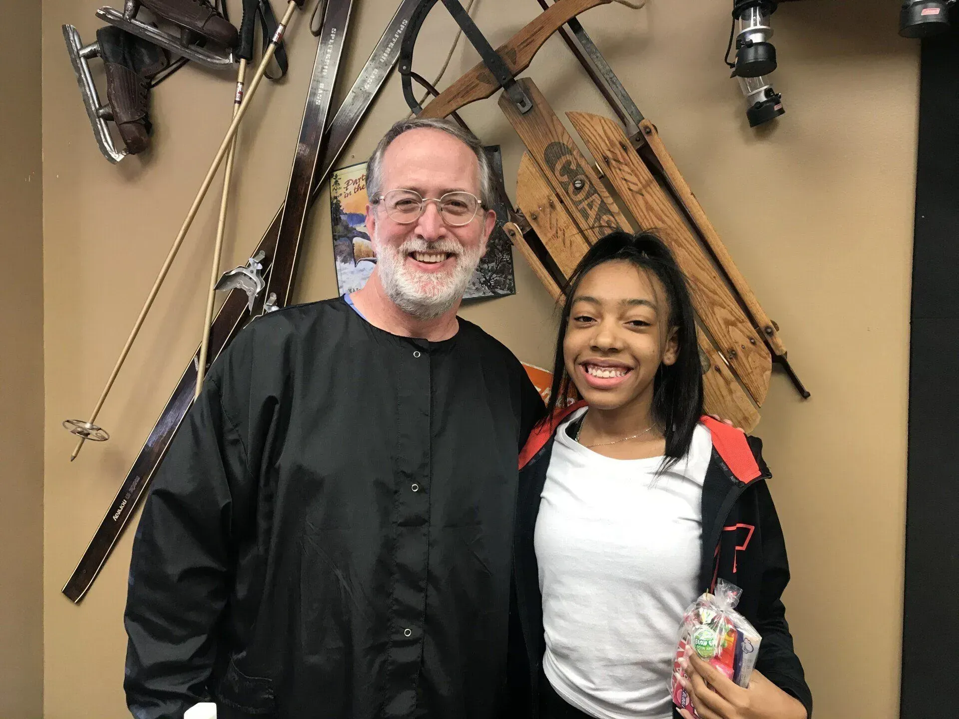 Man and young person smiling in front of wall with decorative skis and sleds.