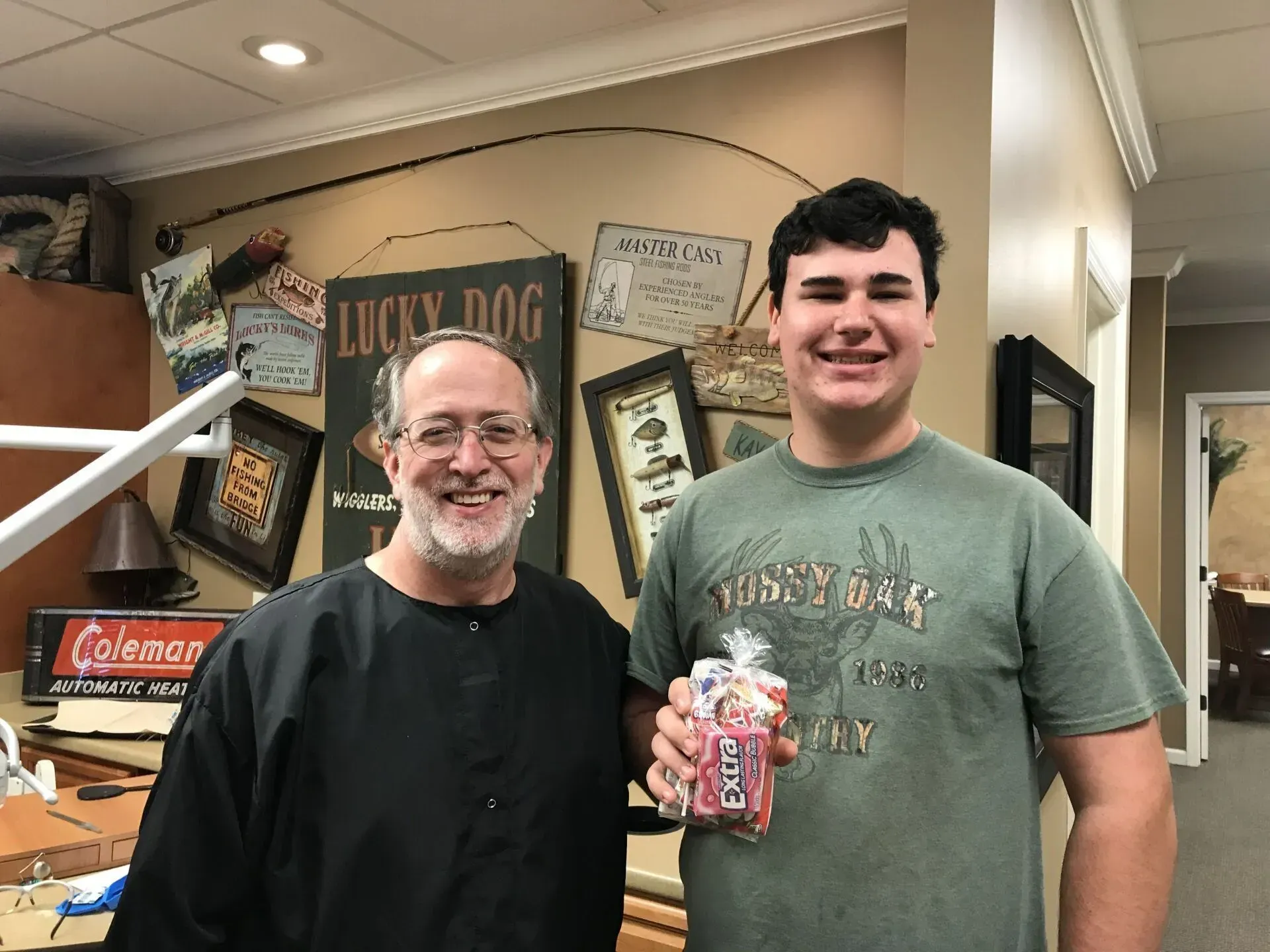 A dentist and a young person smiling, holding a candy bag, in a dental office.