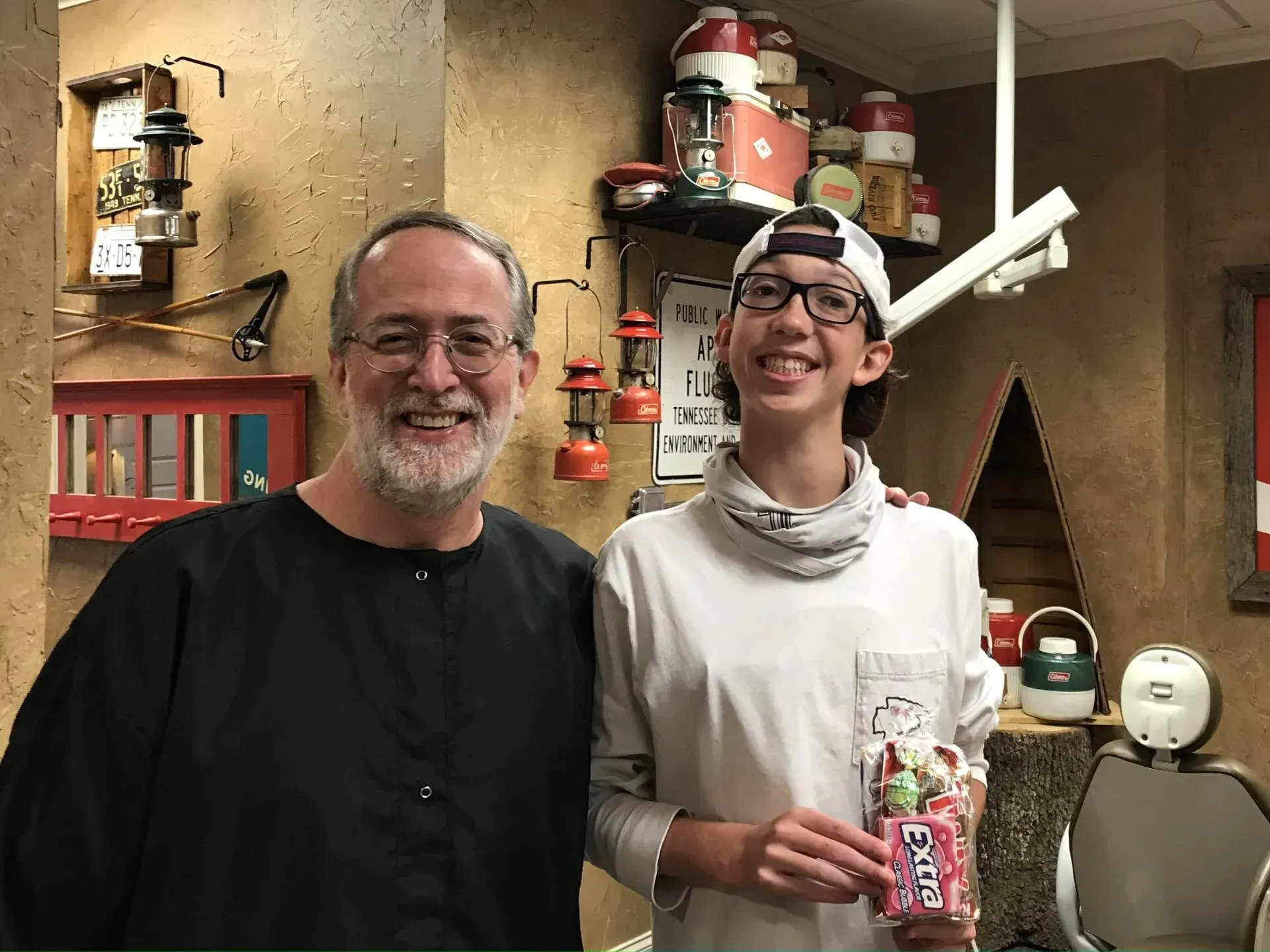Man and teen smiling, standing in a shop with vintage decor; teen holds a product.