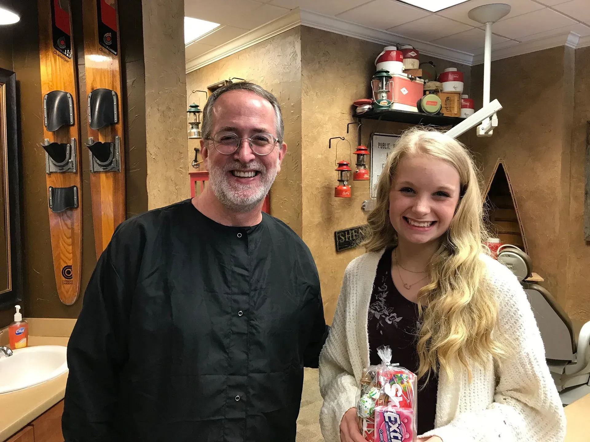 Man in dental scrubs and young woman smiling, holding gift, in a dental office.