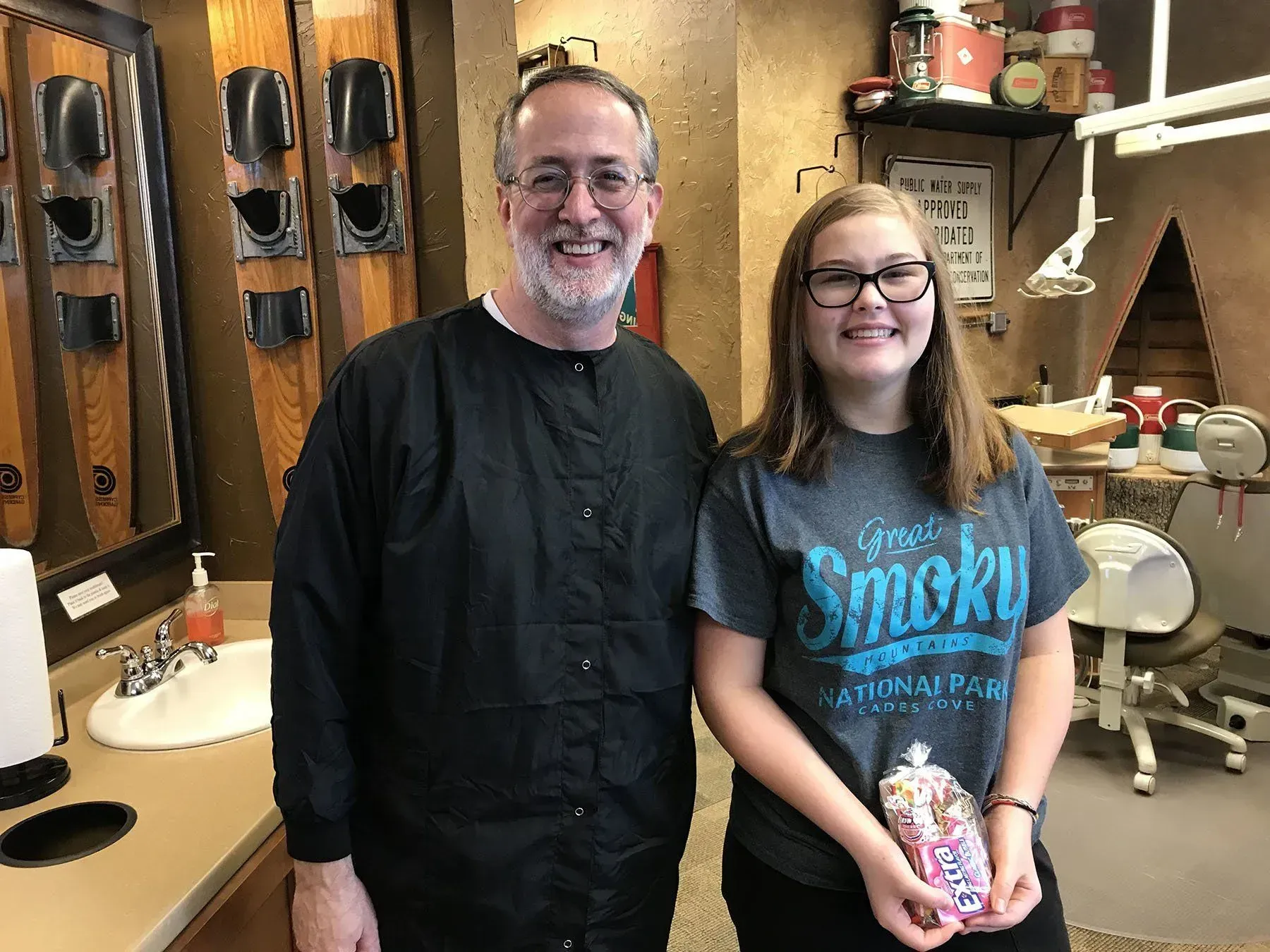 Man in black scrubs and girl in glasses smiling in a dental office. Girl holds candy.