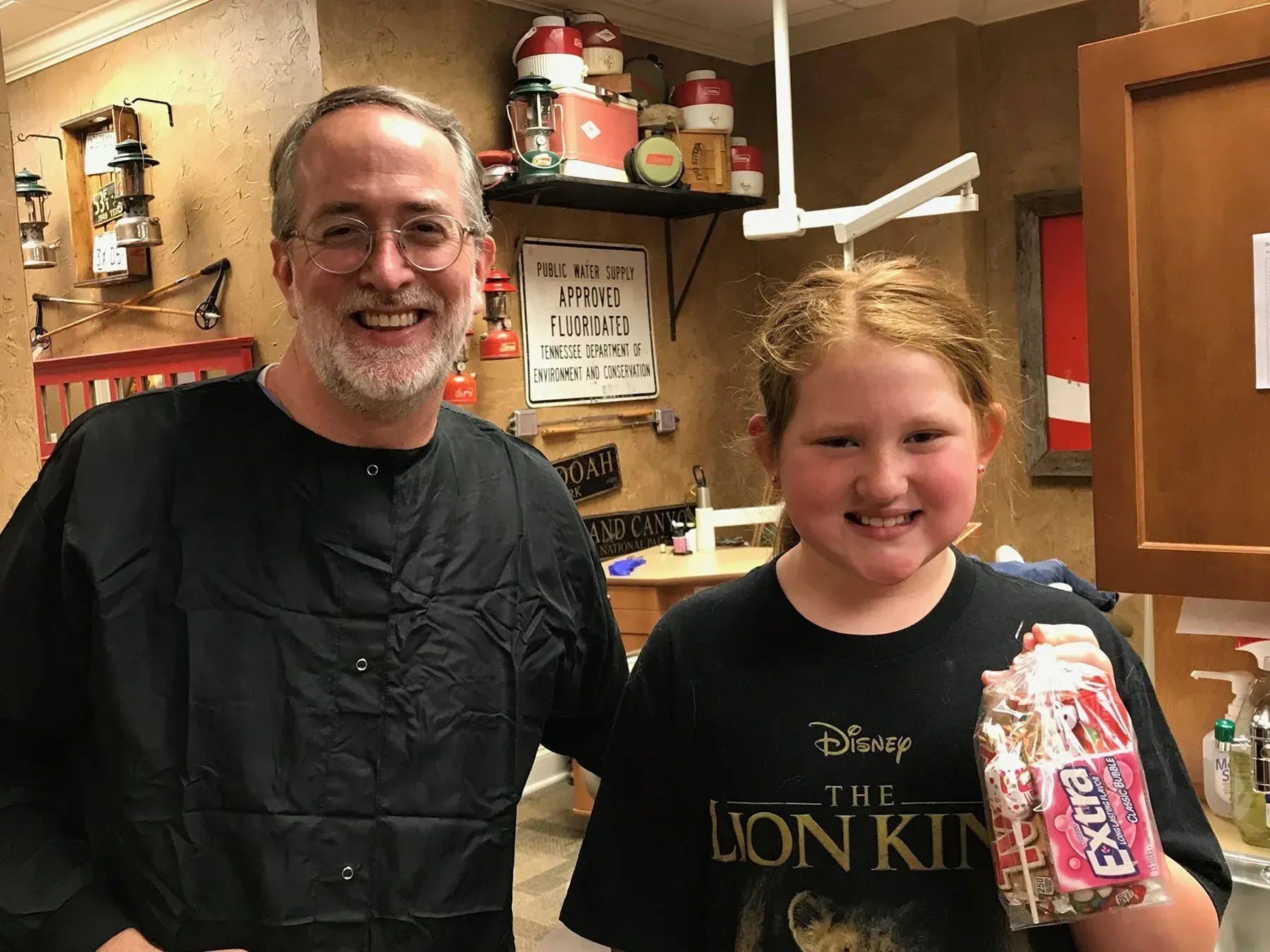 Man with glasses and girl smile, holding juice boxes, posing near shelf with jars, in a shop setting.