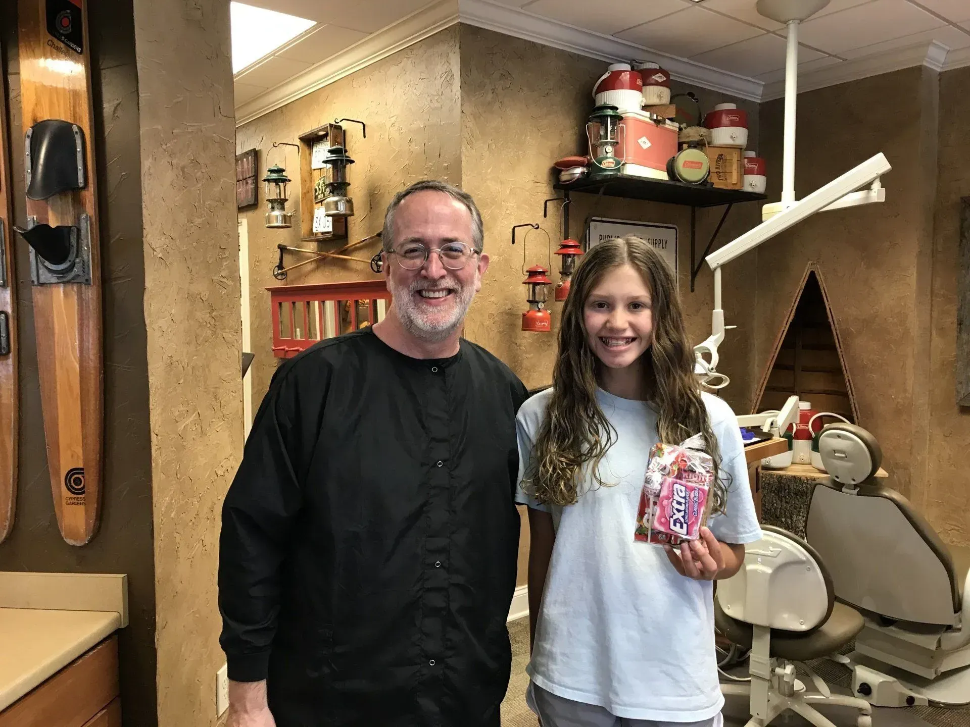 A dentist and a young patient smiling in a dental office. The girl holds a small gift bag.