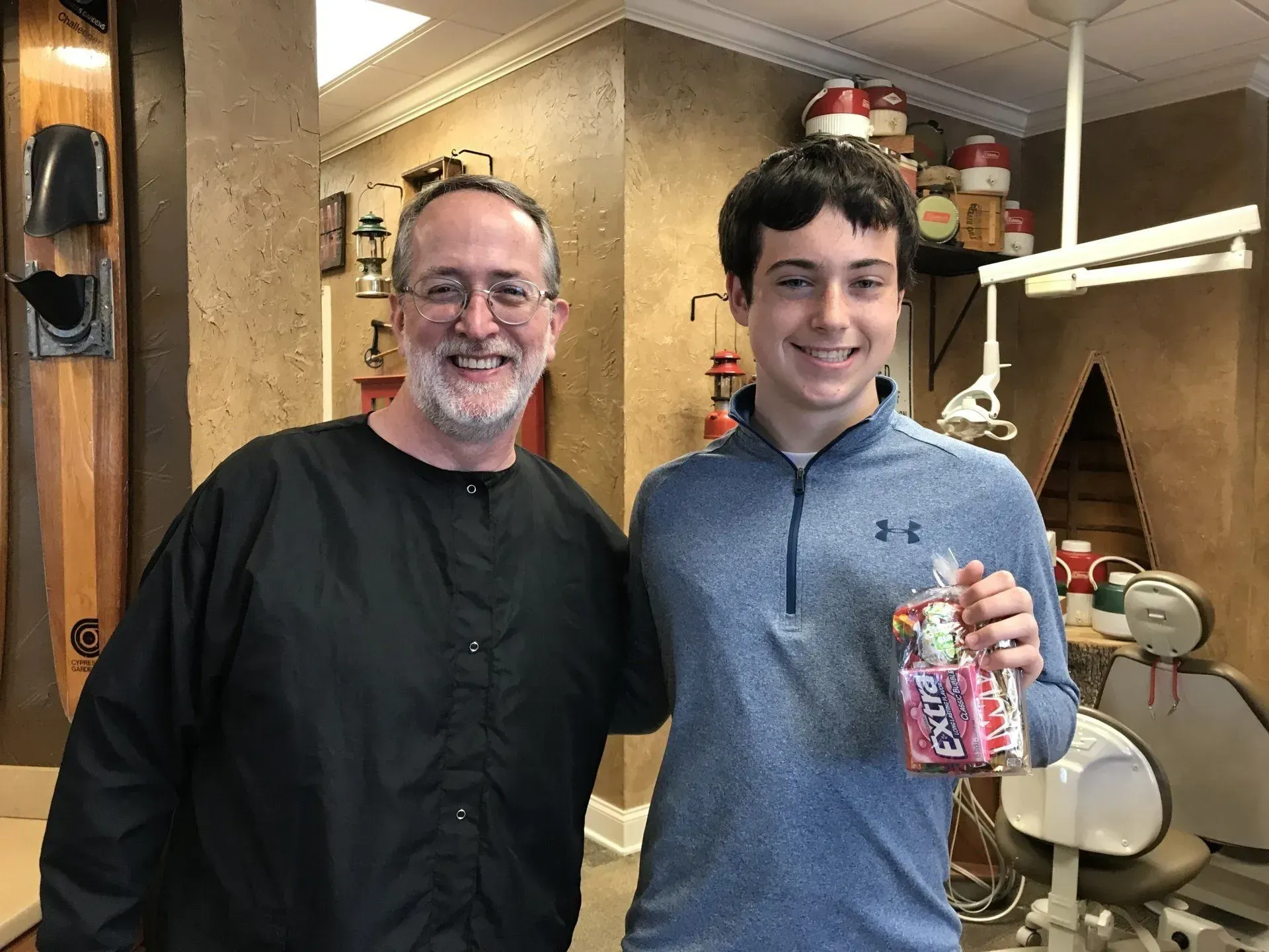 Dentist and patient smiling together in dental office; patient holding a gift.