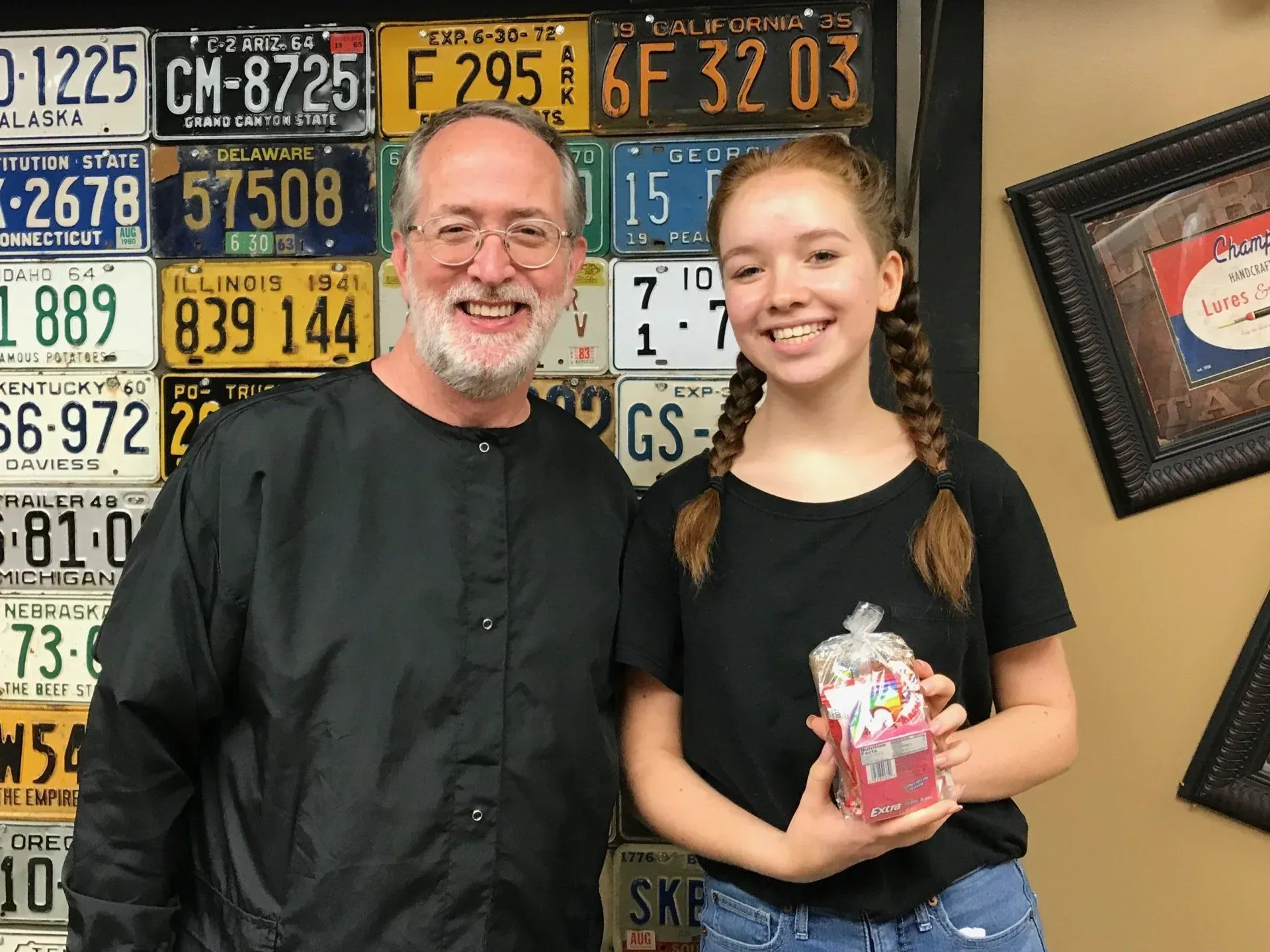 Man and young person smiling, posing with gift. License plates on wall behind.