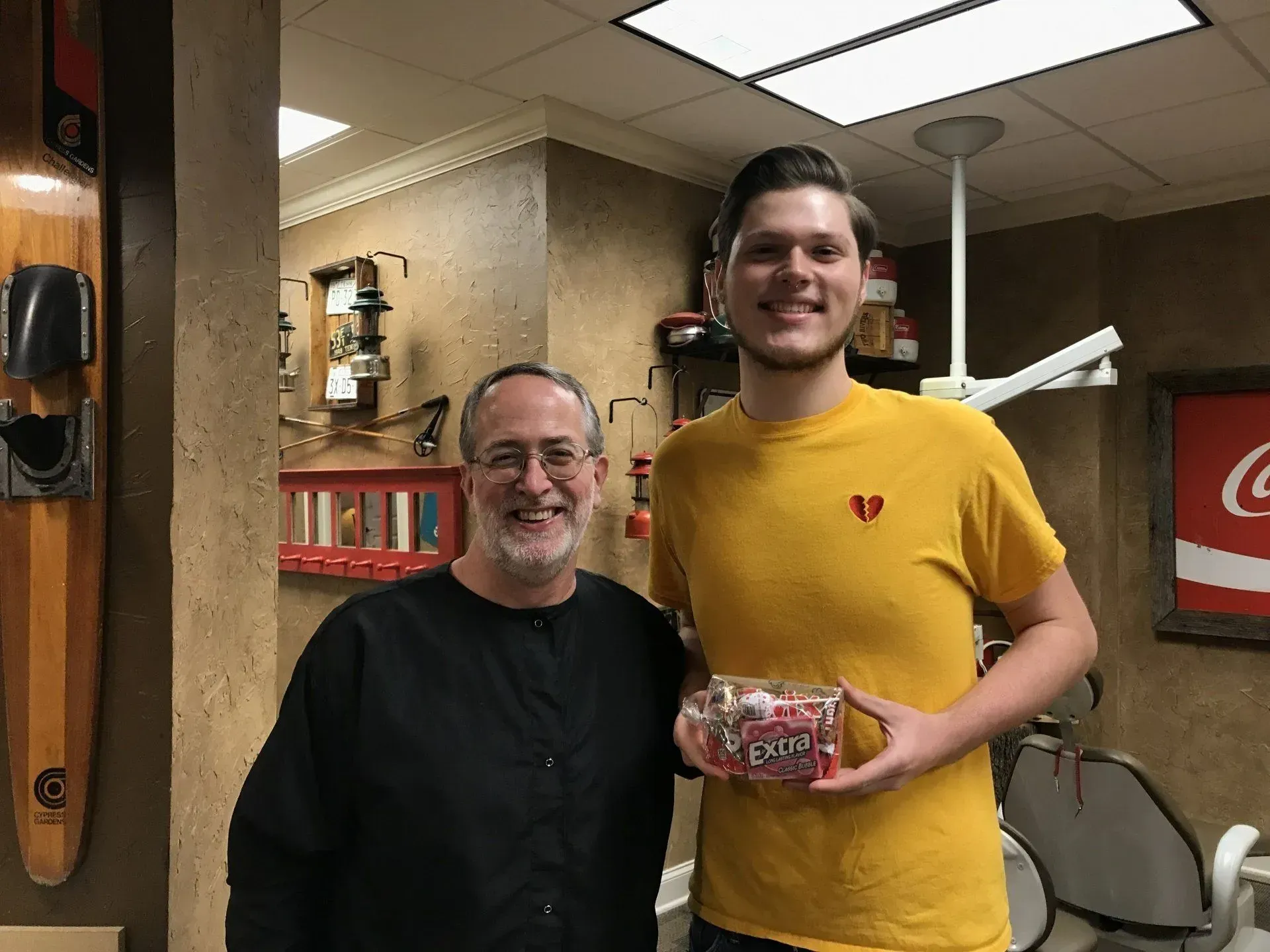 Man and dentist pose, man holds a box of candy, dental office setting.