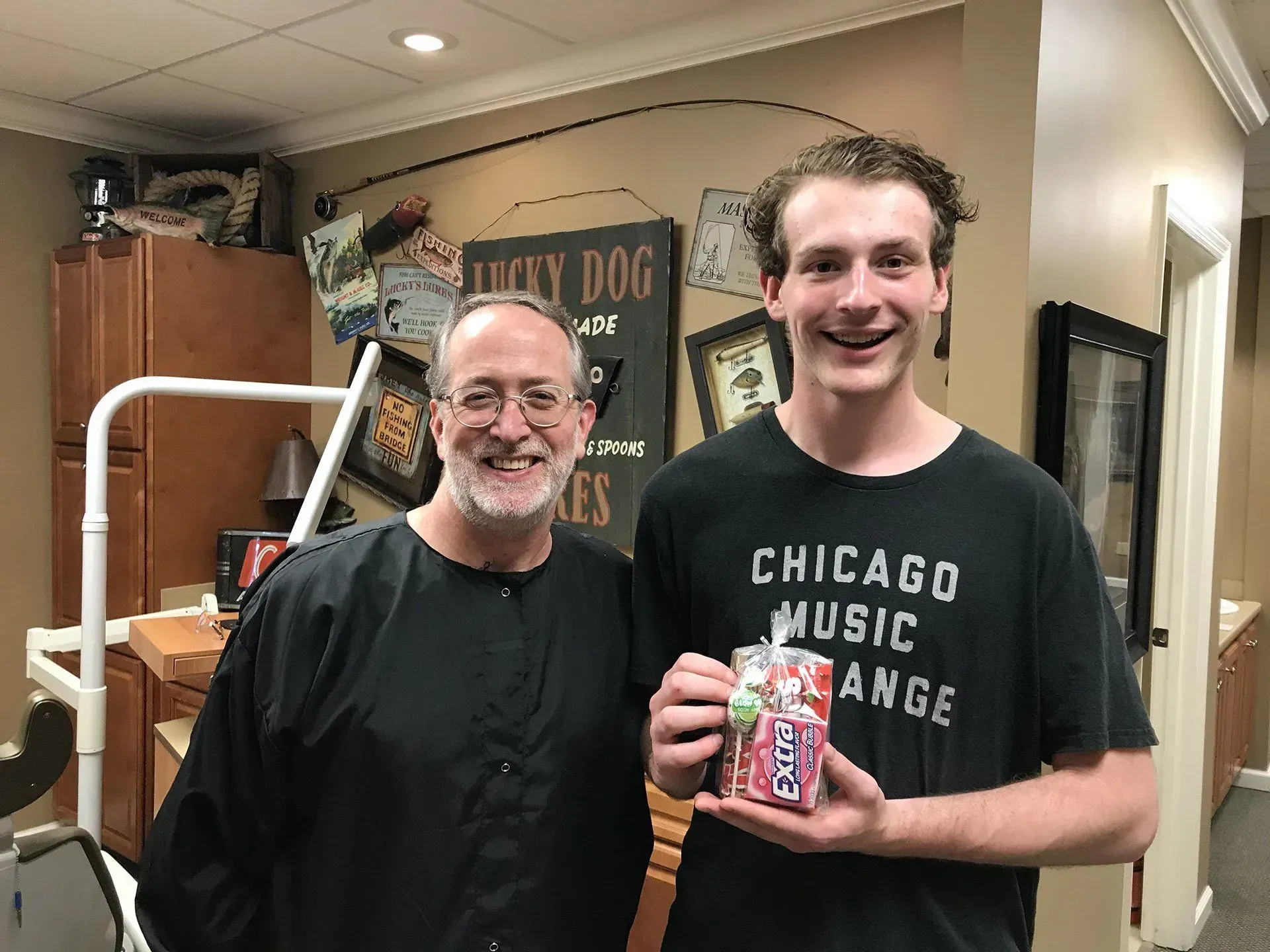 Man with a black cape and young man smiling holding juice box in dentist's office.
