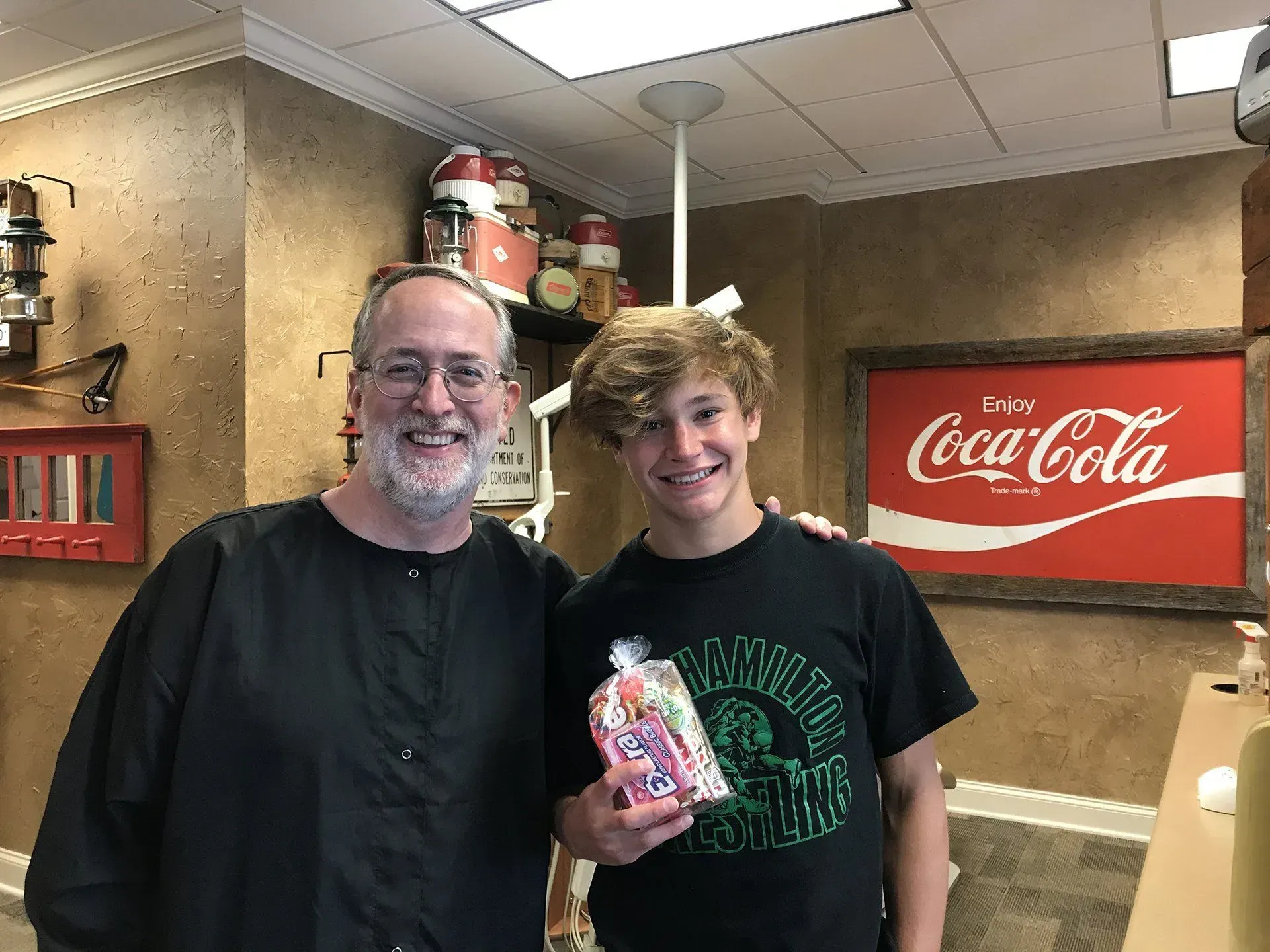 Man and teen pose with candy, near Coca-Cola sign in a shop.
