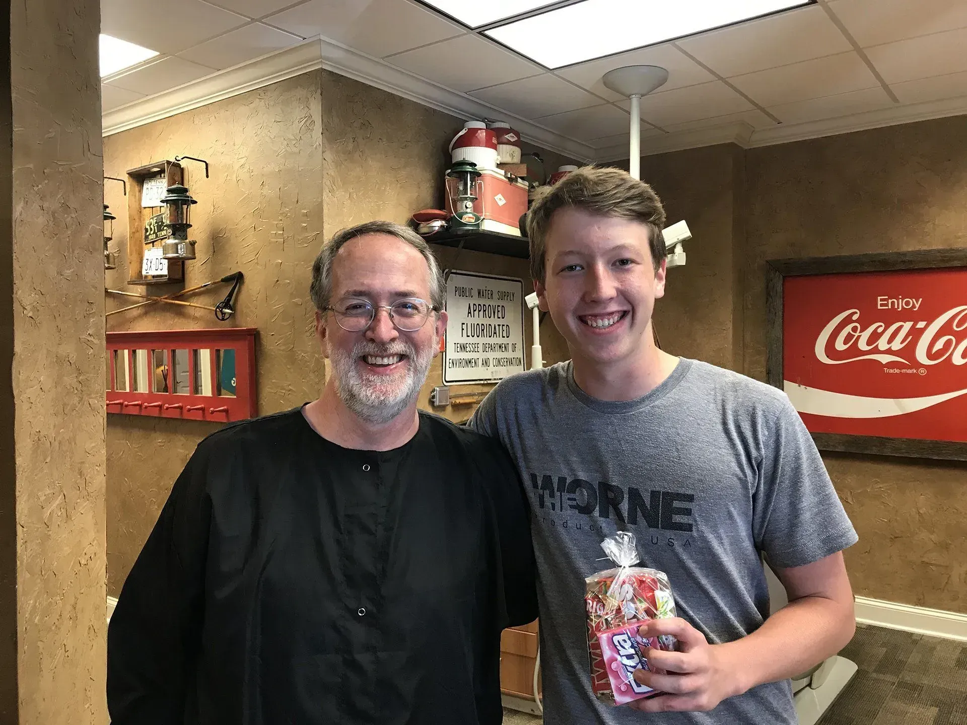 Man and young person smiling and posing together; the young person holds a gift bag. Coca-Cola sign in background.