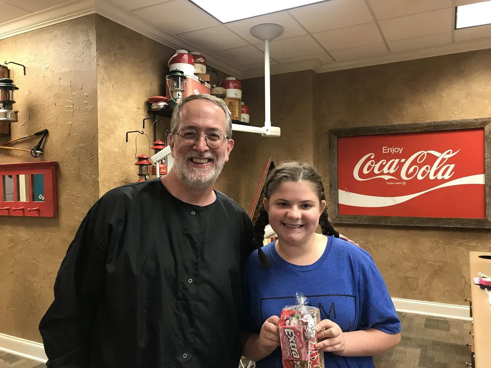 Man and girl smiling, holding treats in room with Coca-Cola sign.