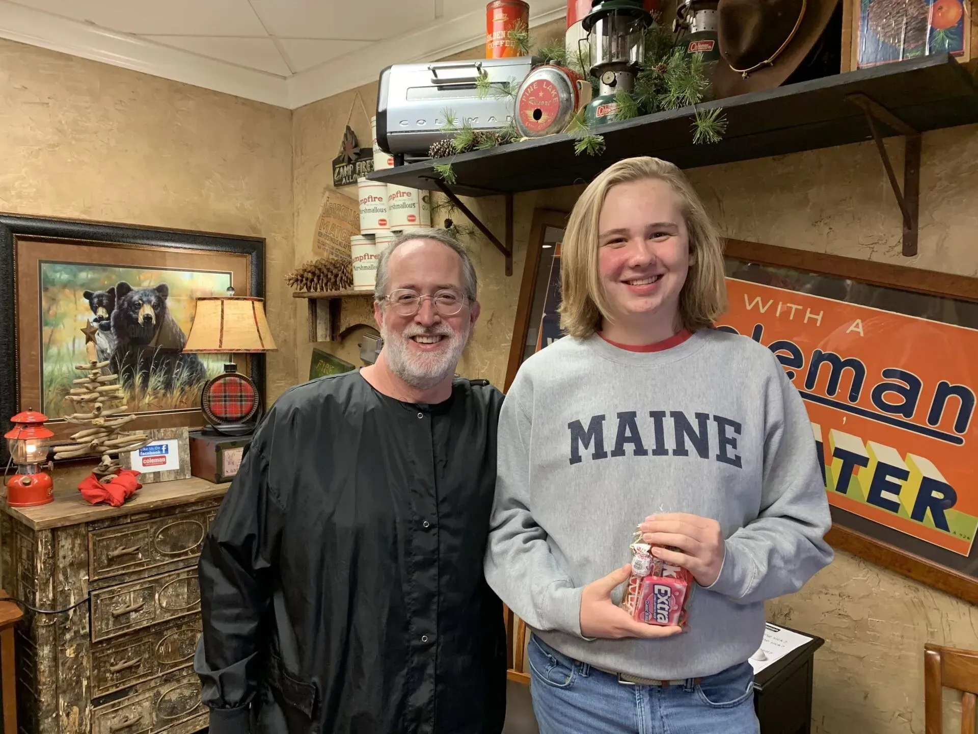 Man and teen smiling, holding object, standing in store with camping decor.