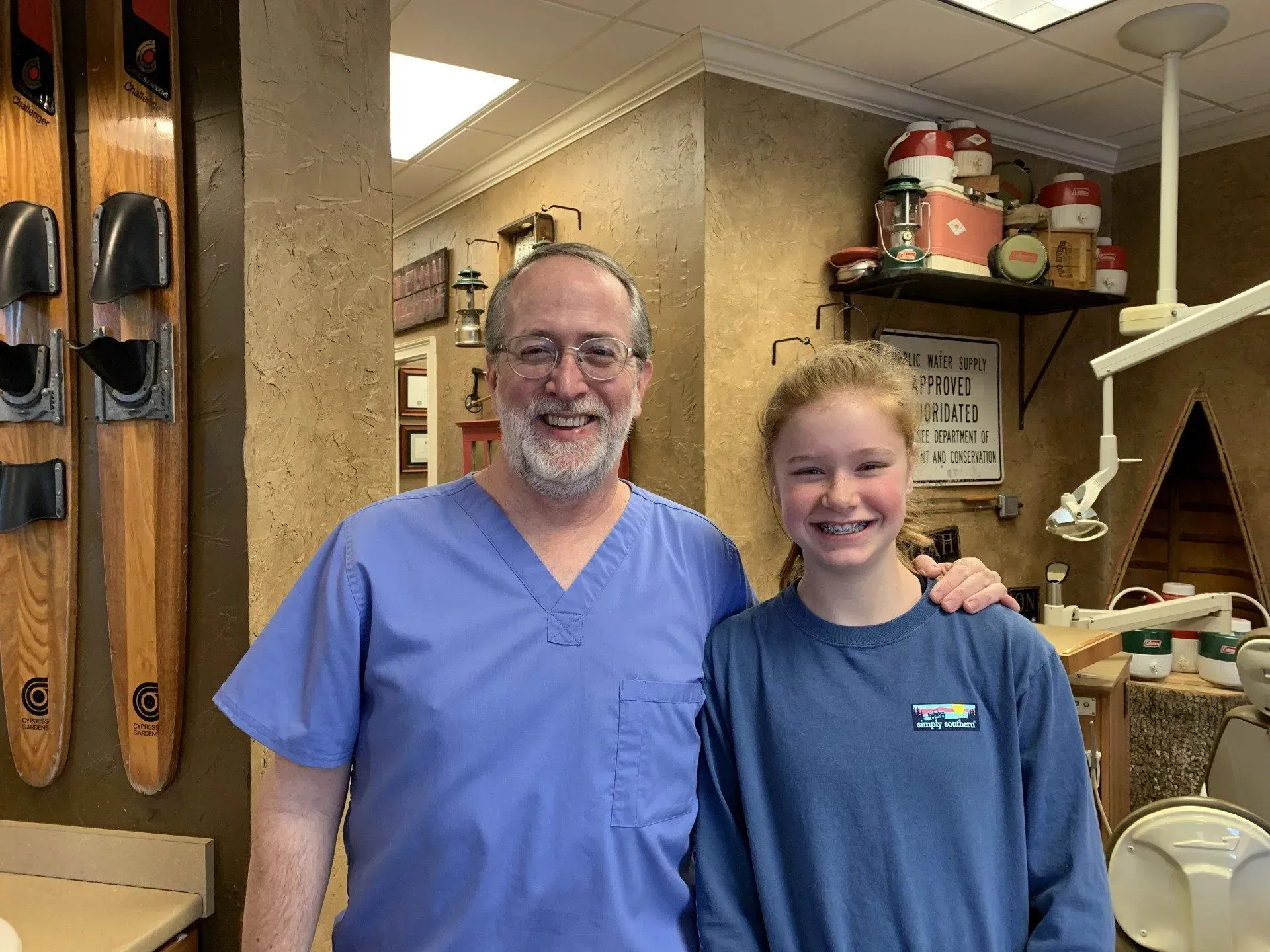 Man in blue scrubs and young person smiling in dental office setting.