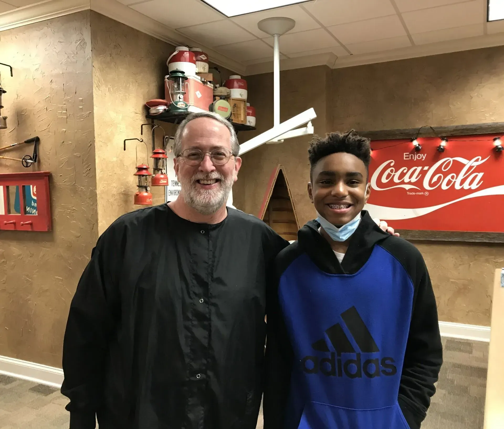 Man and teen smiling next to each other in a decorated room with a Coca-Cola sign.