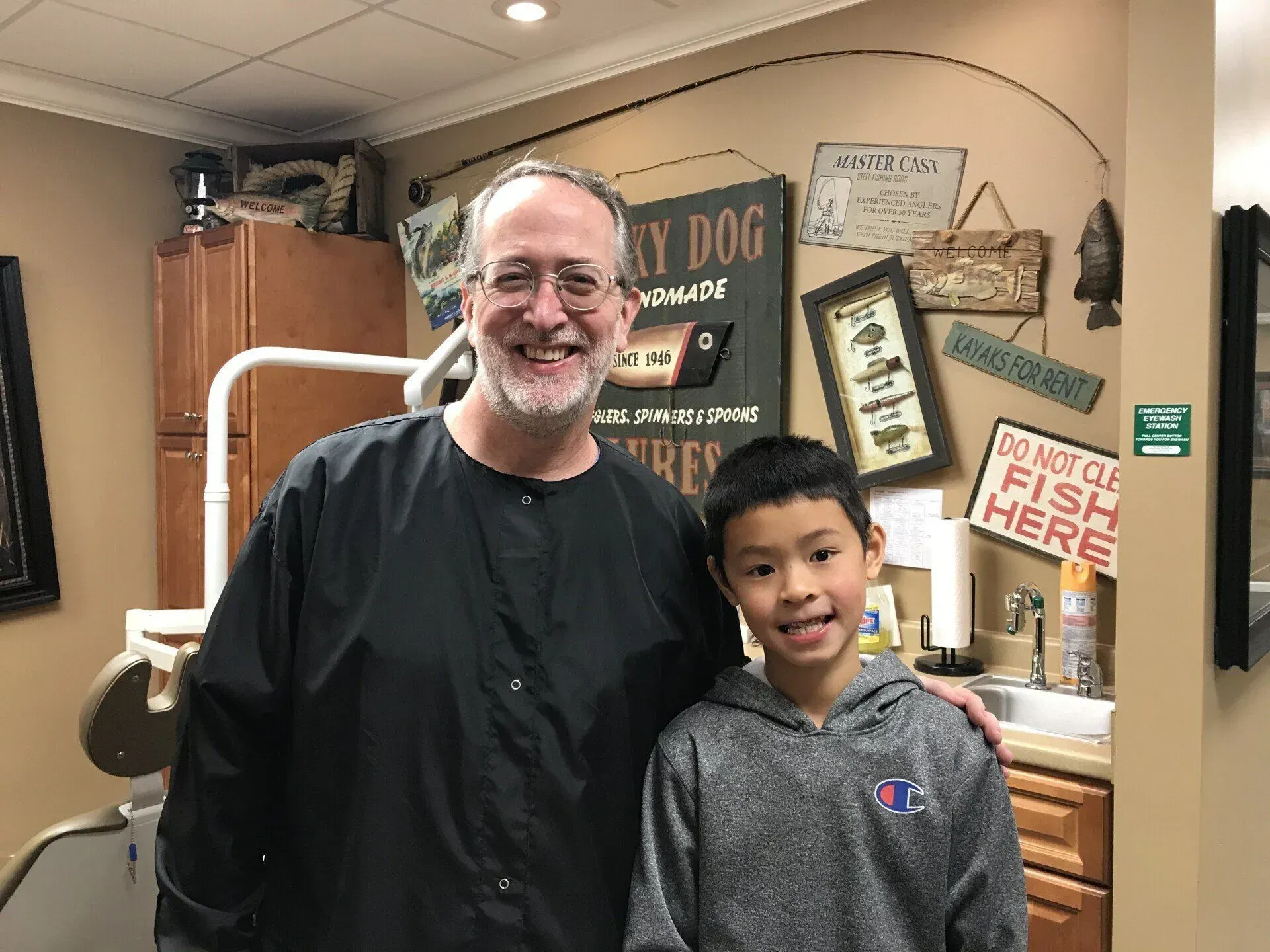 Dentist with smiling young patient at a dental office, posing near a decorative fishing theme wall.