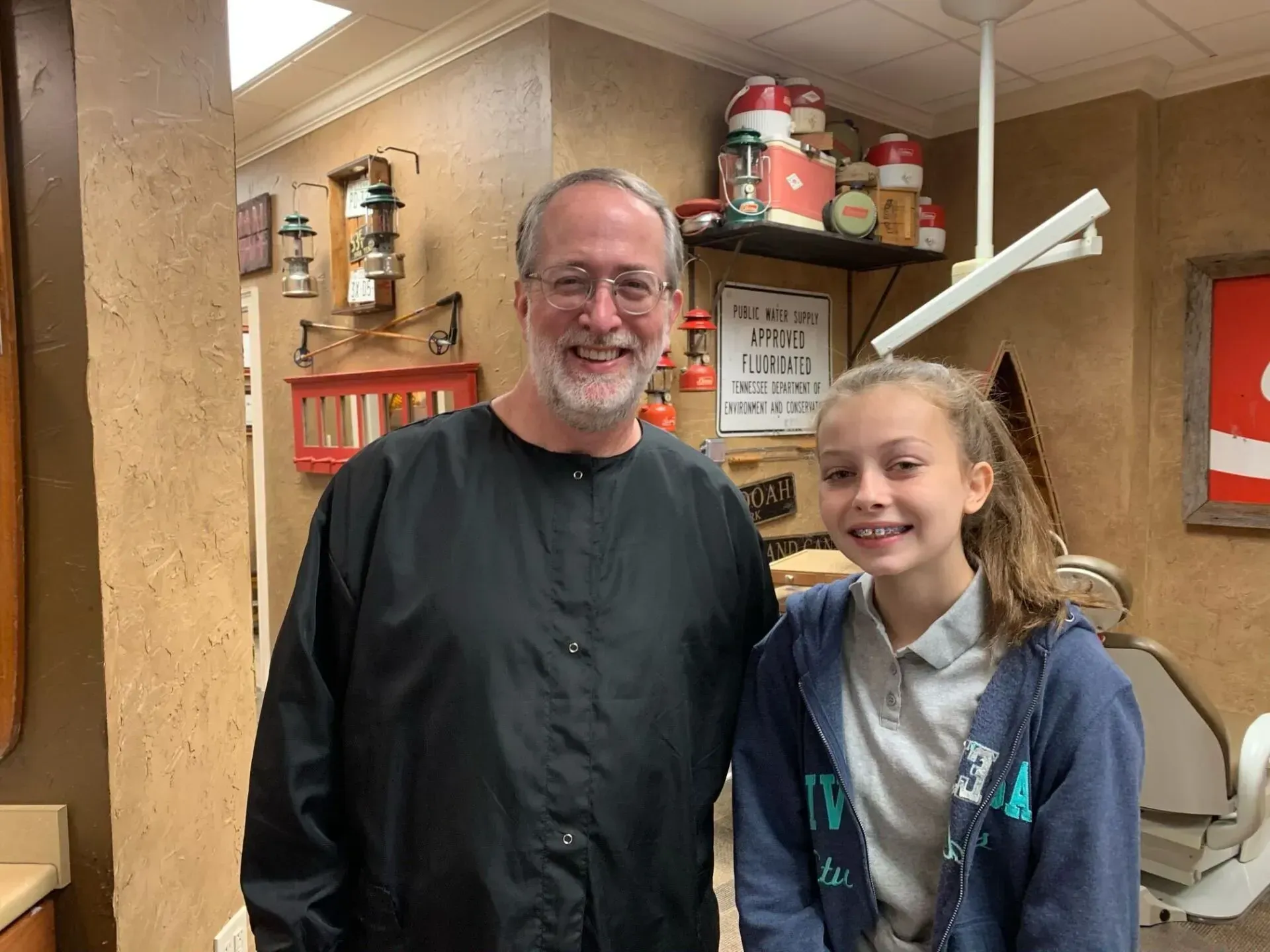Dentist and patient smiling in dental office. Rustic decor, exposed brick, jars on shelf.