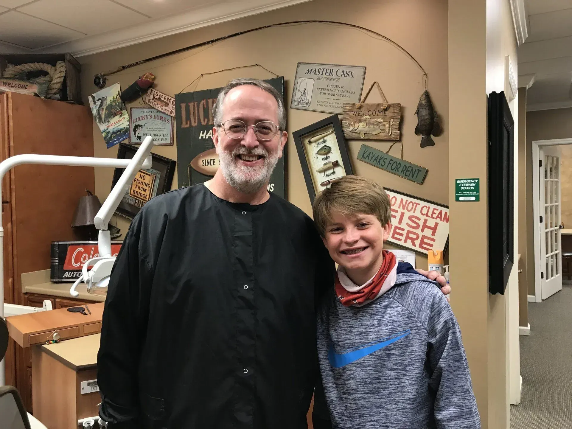 Man and boy pose in a dentist's office with fishing decor on the wall. Both are smiling.