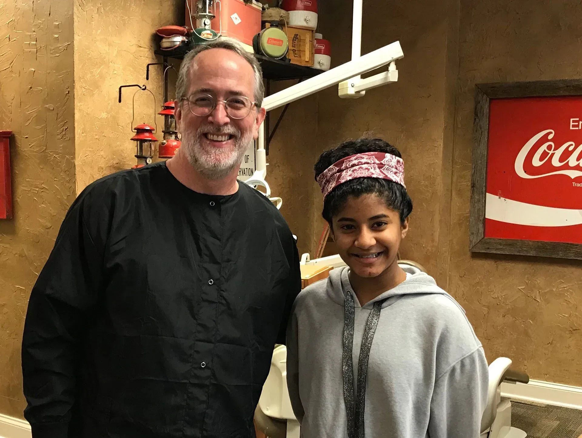 Dentist and young patient smiling in a dental office, with a Coca-Cola sign in the background.