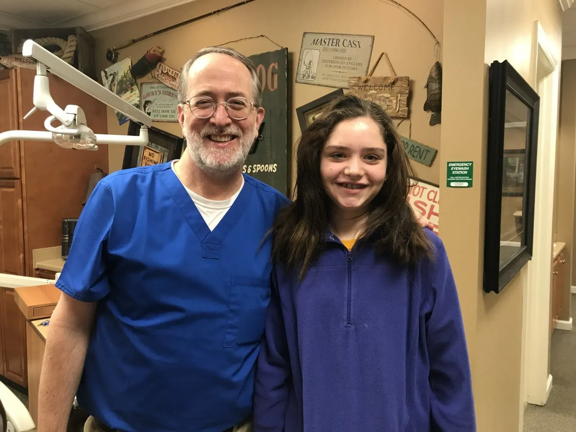 Dentist in blue scrubs and young person smiling in dental office.