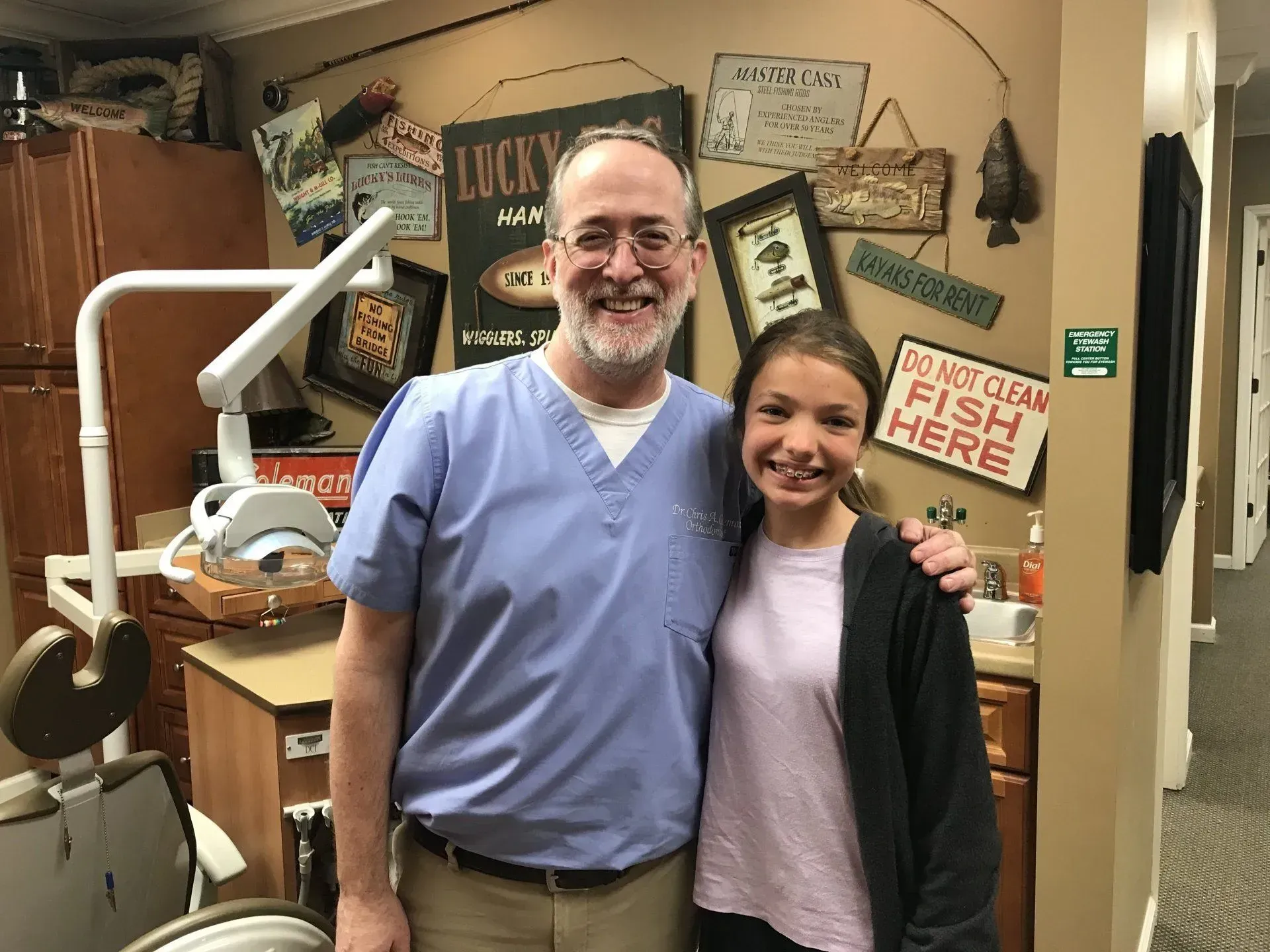 Dentist with a patient, smiling in a dental office. Wall decor and dental equipment are visible.
