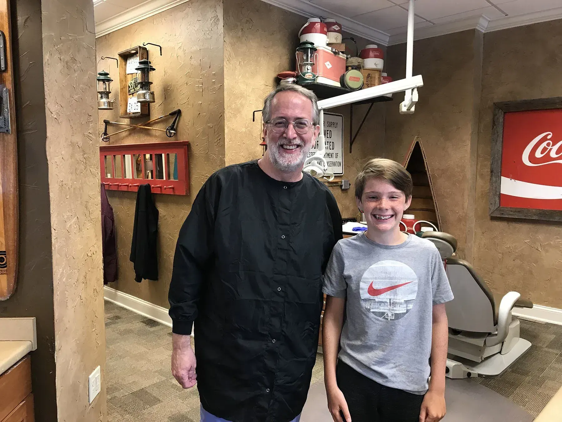 A man and a boy smiling in a dental office. The man is wearing black and the boy has a gray shirt.