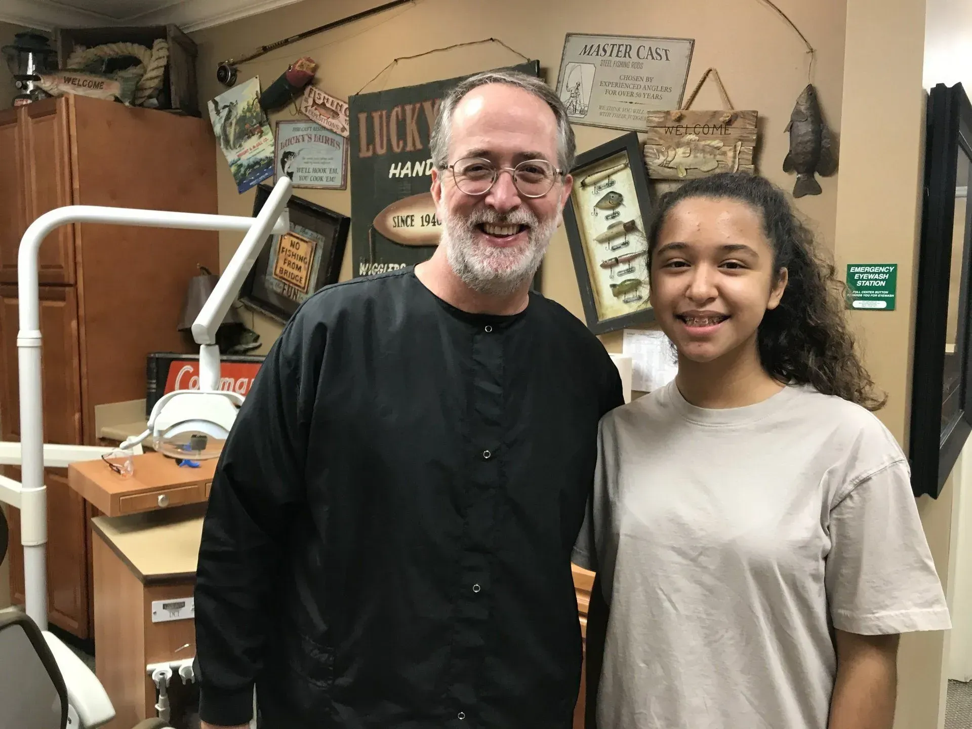 Man and young person smiling next to each other in a dental office. Wall decor visible.