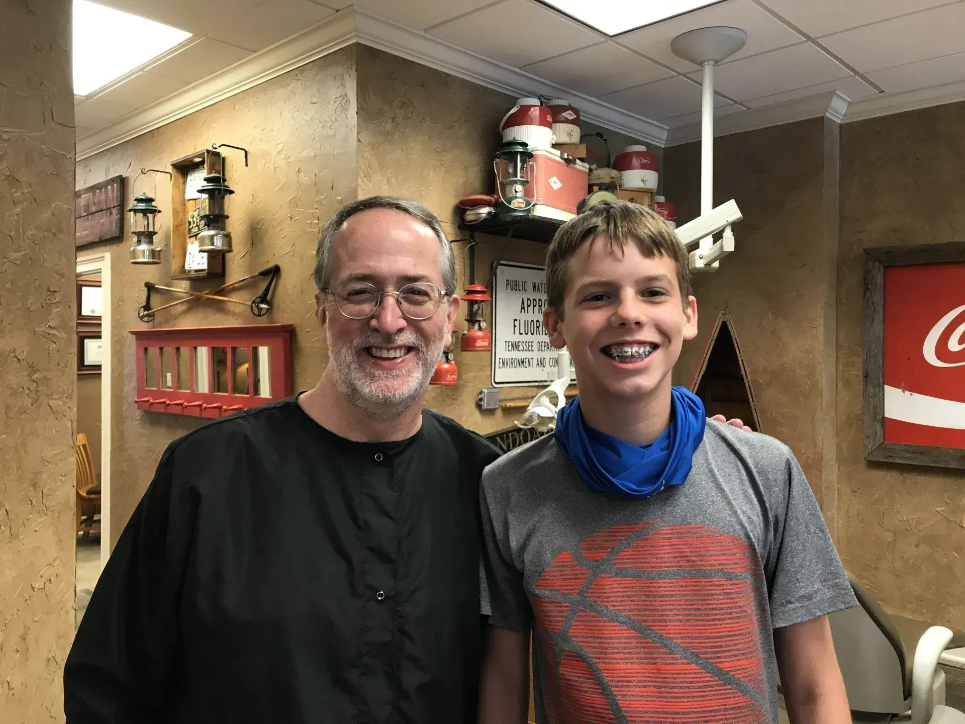 Dentist and boy with braces smiling in a dental office. Rustic decor, Coca-Cola sign.
