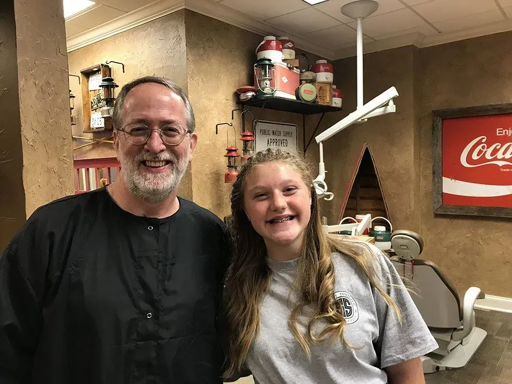Man and girl smile in a vintage barber shop, near a barber chair and Coca-Cola sign.