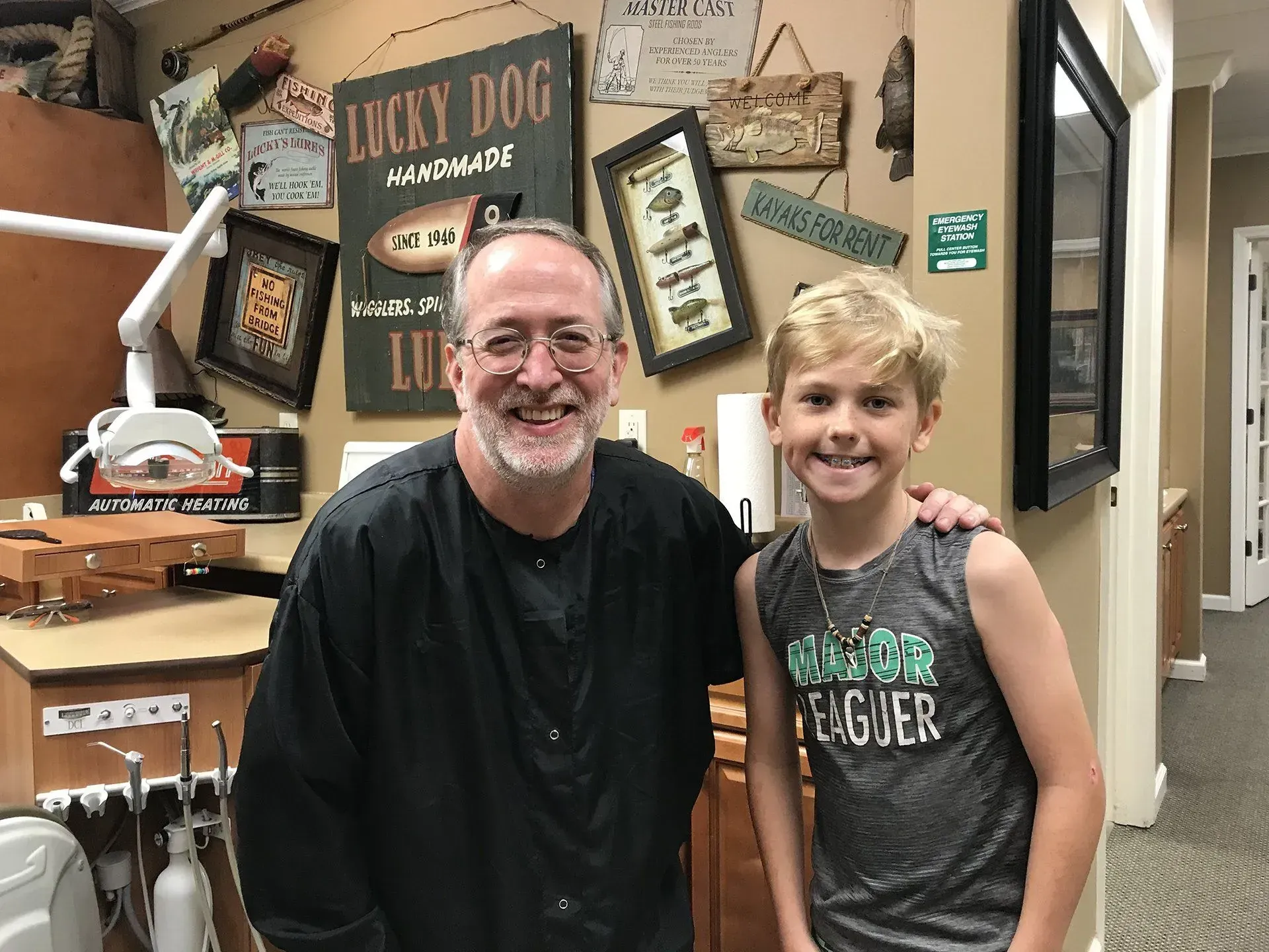 Man and boy smile together in a dental office. The man has an arm around the boy's shoulder.