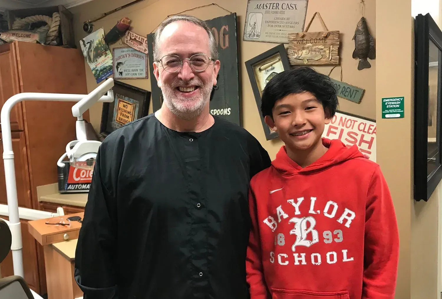 Man in black smock and young person in red Baylor sweatshirt smiling together in a dental office.