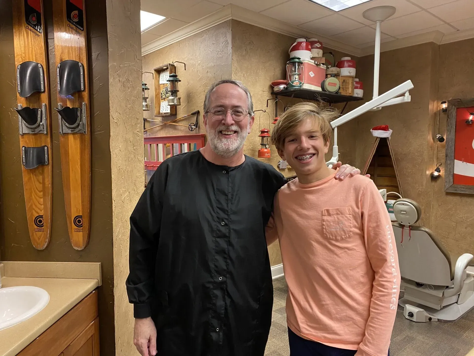 Man in black work attire and a smiling teen pose in a dental office.