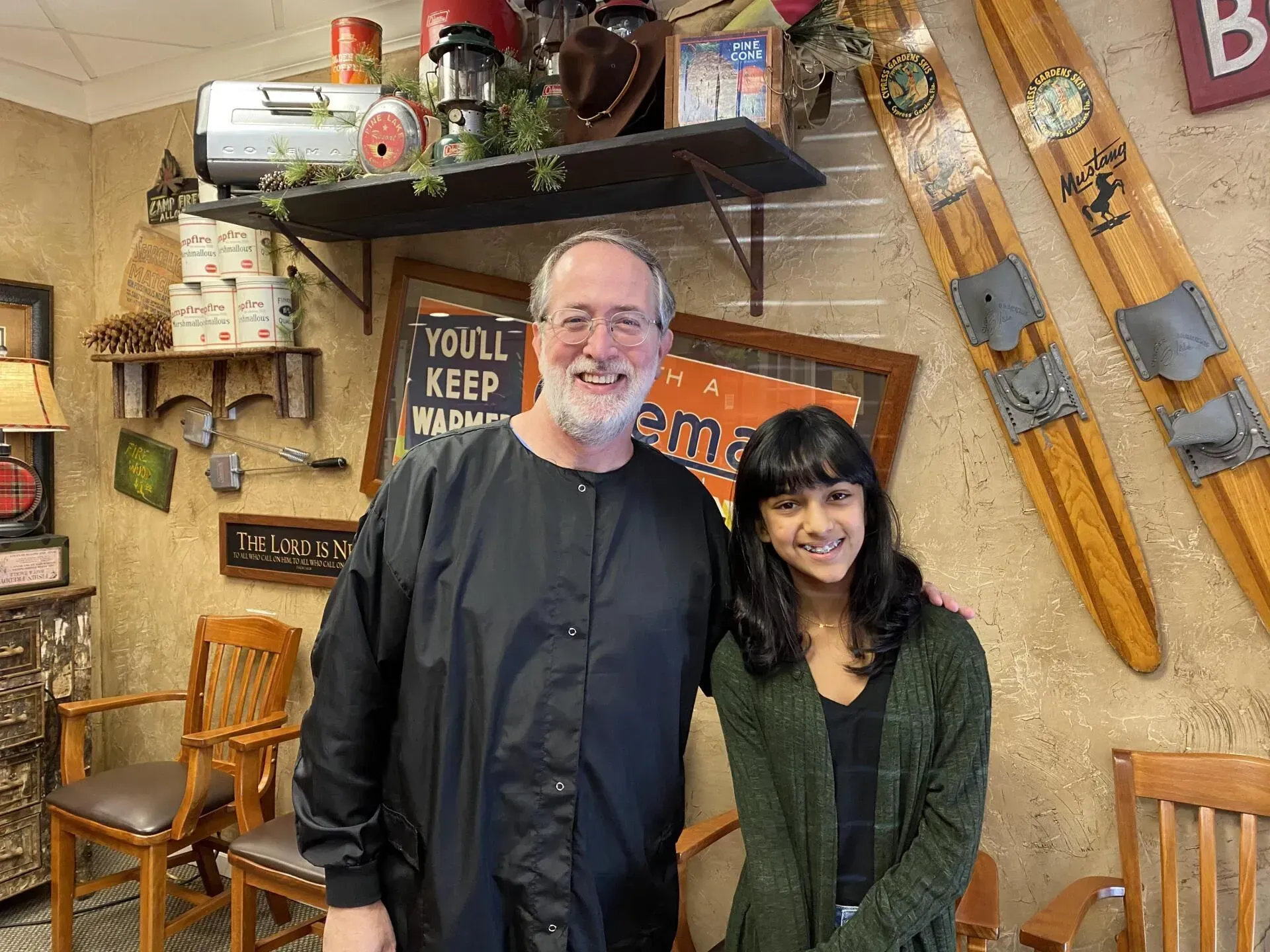 Two people smiling, standing near decor. A man in black clothing and a woman in a green sweater.
