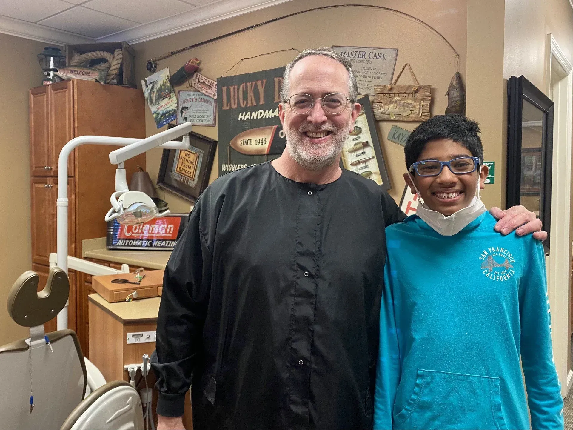 Dentist and young patient smiling in a dental office; dentist has arm around patient.