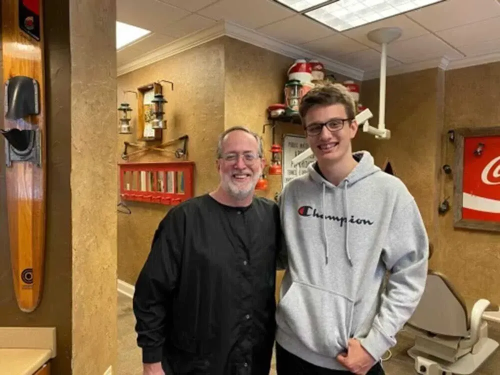 Two men pose in a dental office. One in a gray 