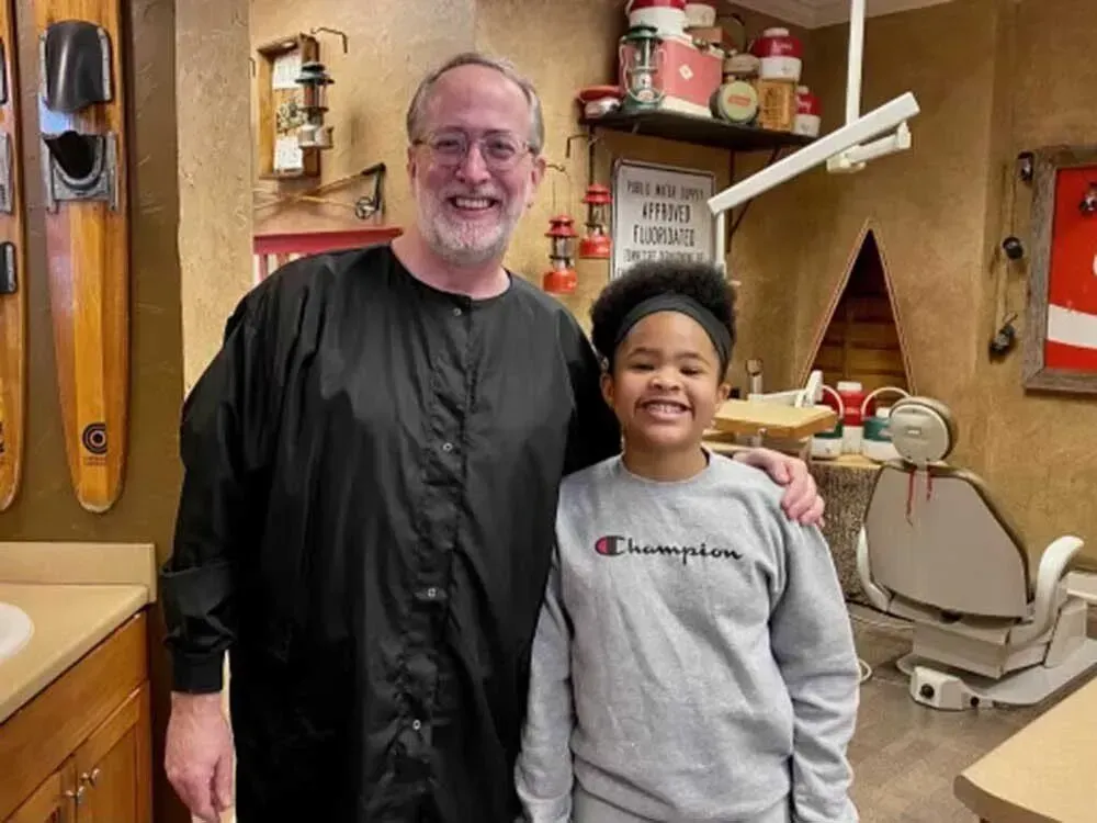 Dentist with patient in a dental office. Both smile, arm around the girl. Rustic decor.