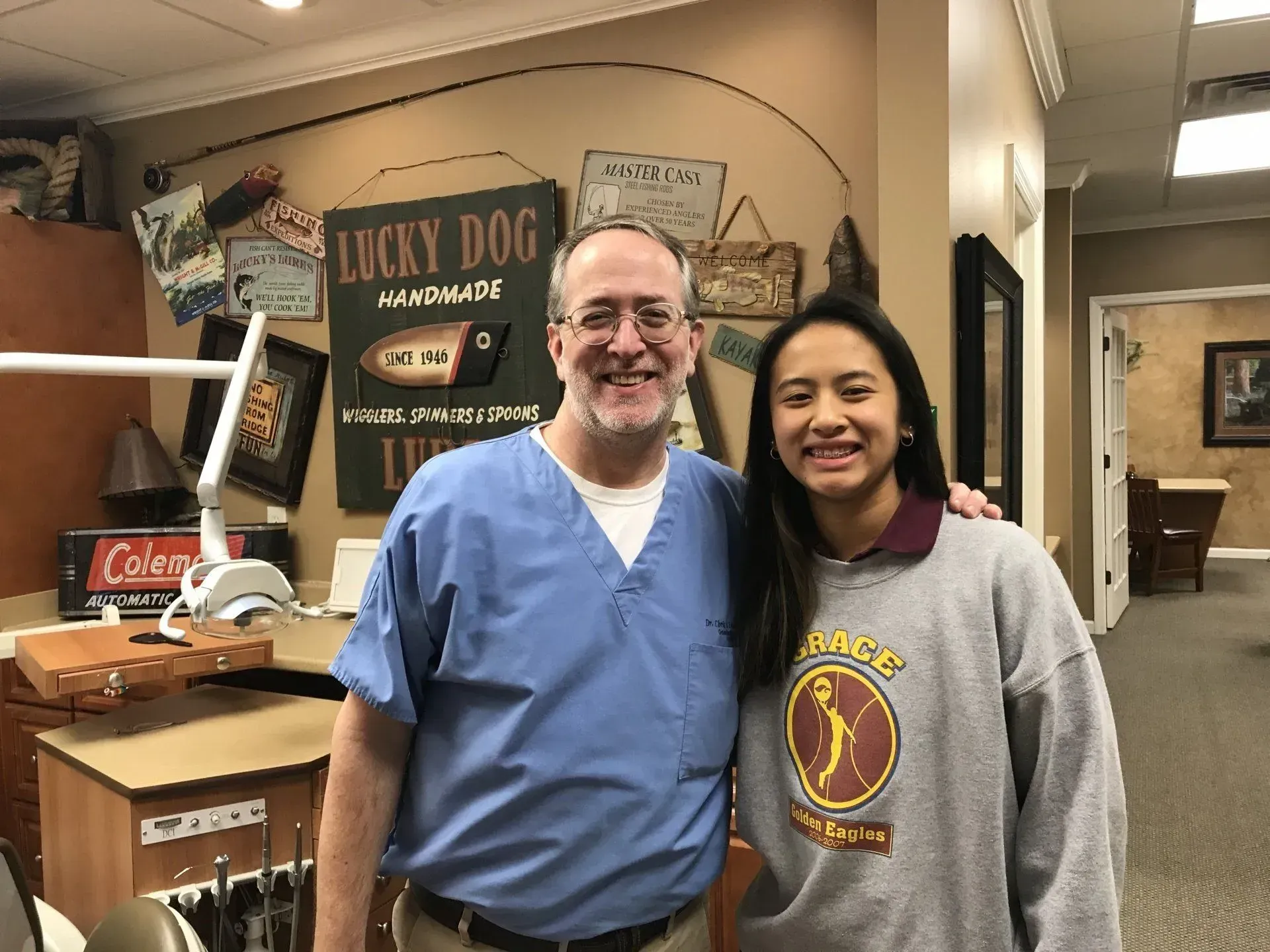 A man in scrubs and a young person in a sweatshirt smile together in a dental office.