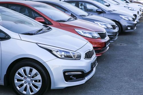 Row of parked cars in a dealership lot, including silver, red, and dark-colored vehicles