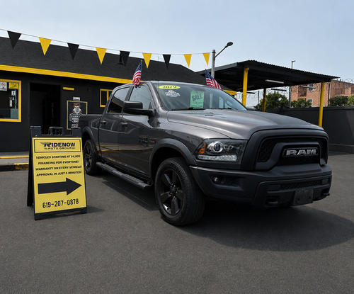 Black RAM truck parked at a car lot with yellow pennant flags and a sale sign.