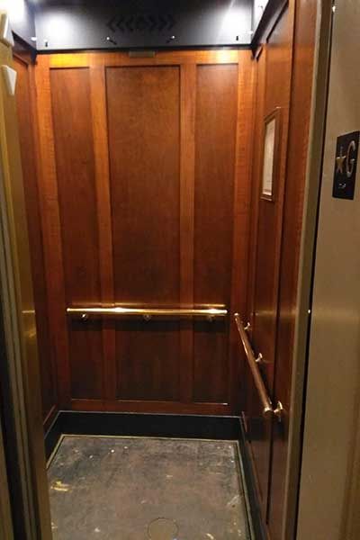 The inside of an elevator with wood paneling and gold handles