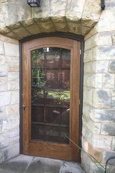 A wooden door with a glass window is on a stone wall.