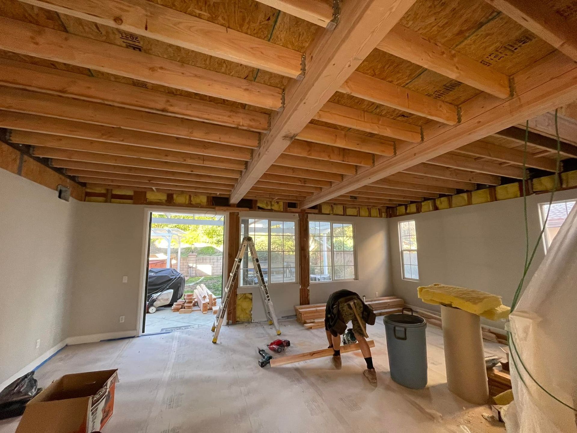 Interior construction scene with exposed wooden beams, insulation, and a person working.