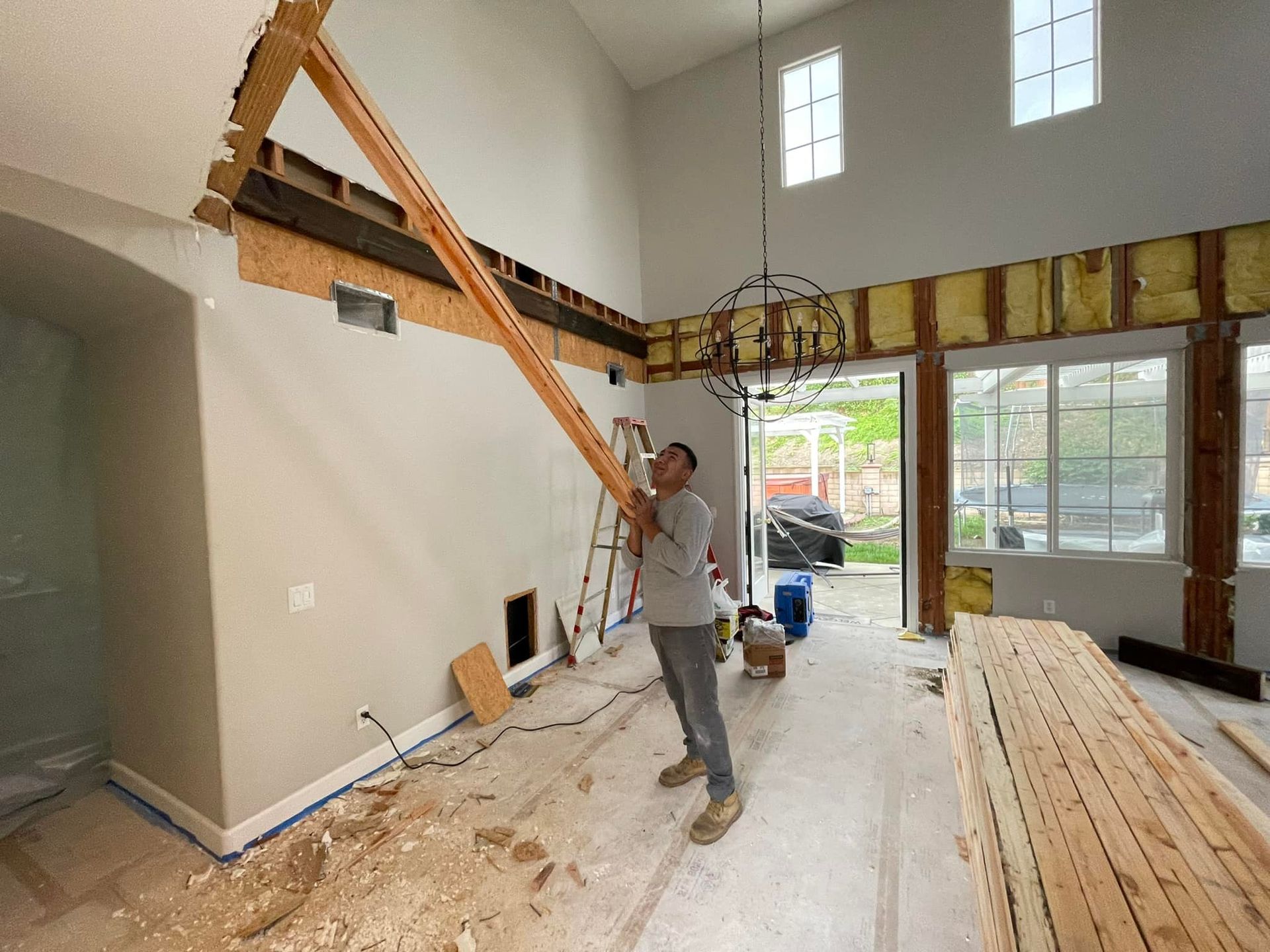 Man holding wooden beam in room under construction. Exposed wall, high ceiling, natural light.