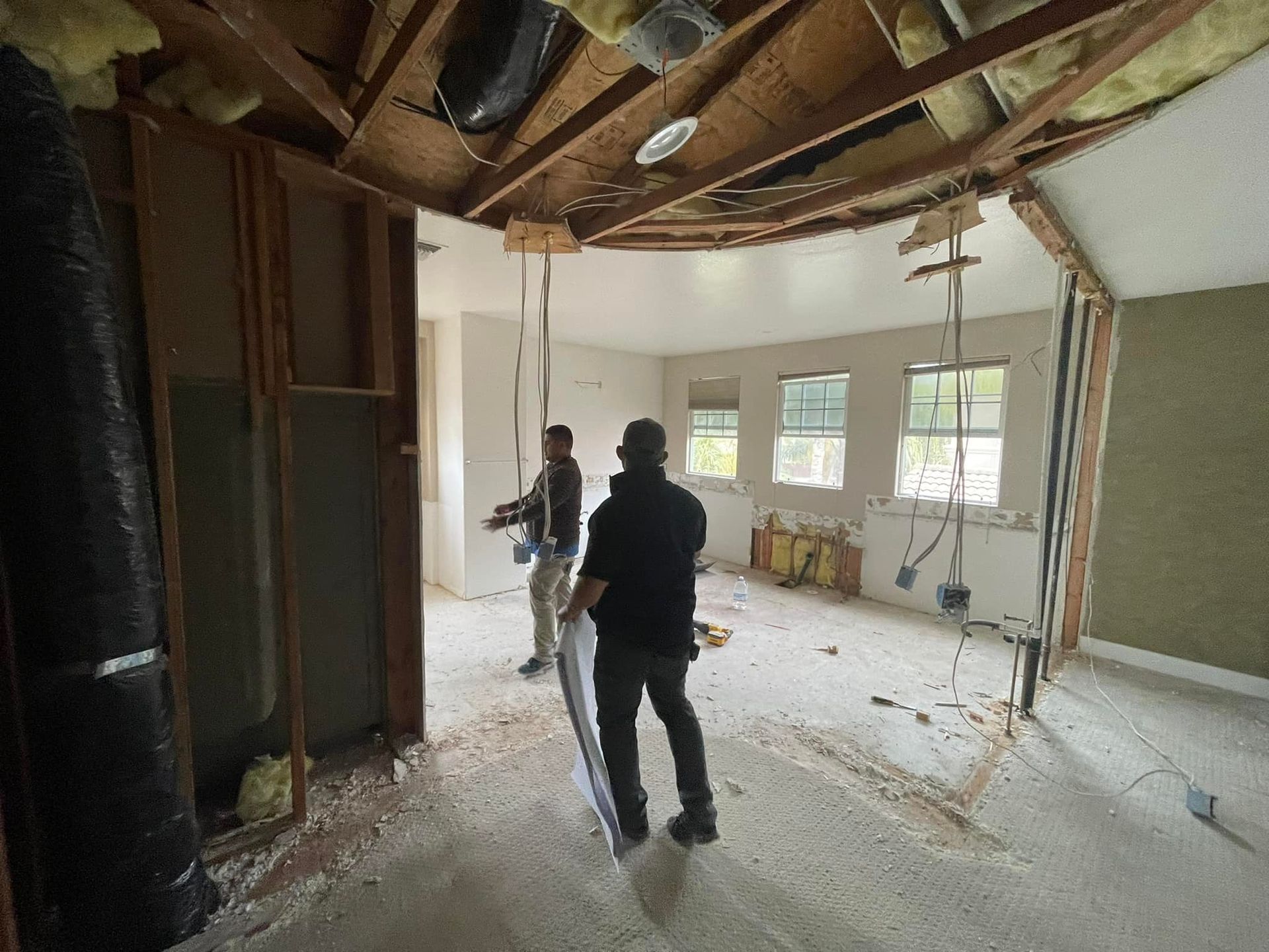 Two people renovating a room; walls and ceiling partially removed.
