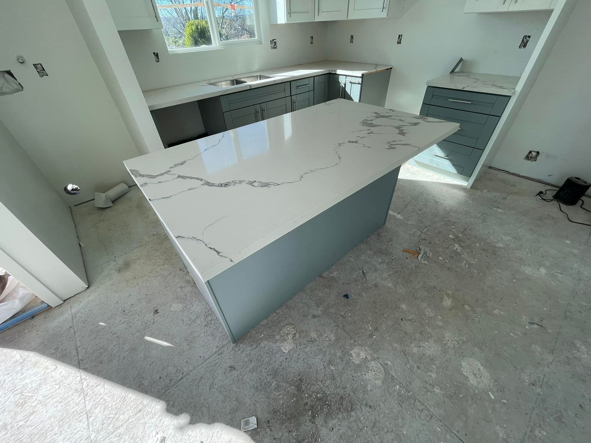 Kitchen under construction with gray cabinets, white countertops and island.