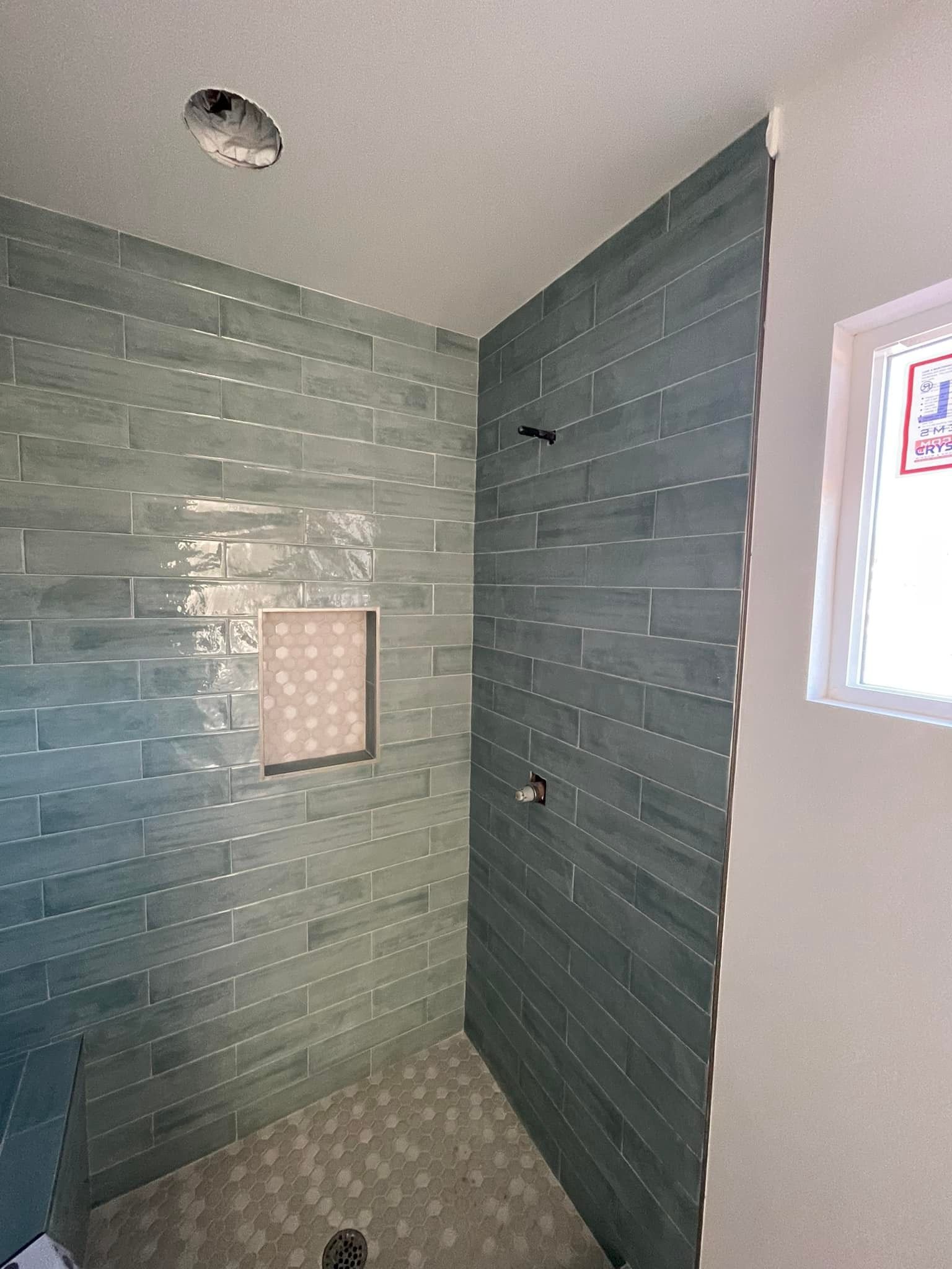 Shower with blue-green tile walls, a built-in shelf, and a white framed window.