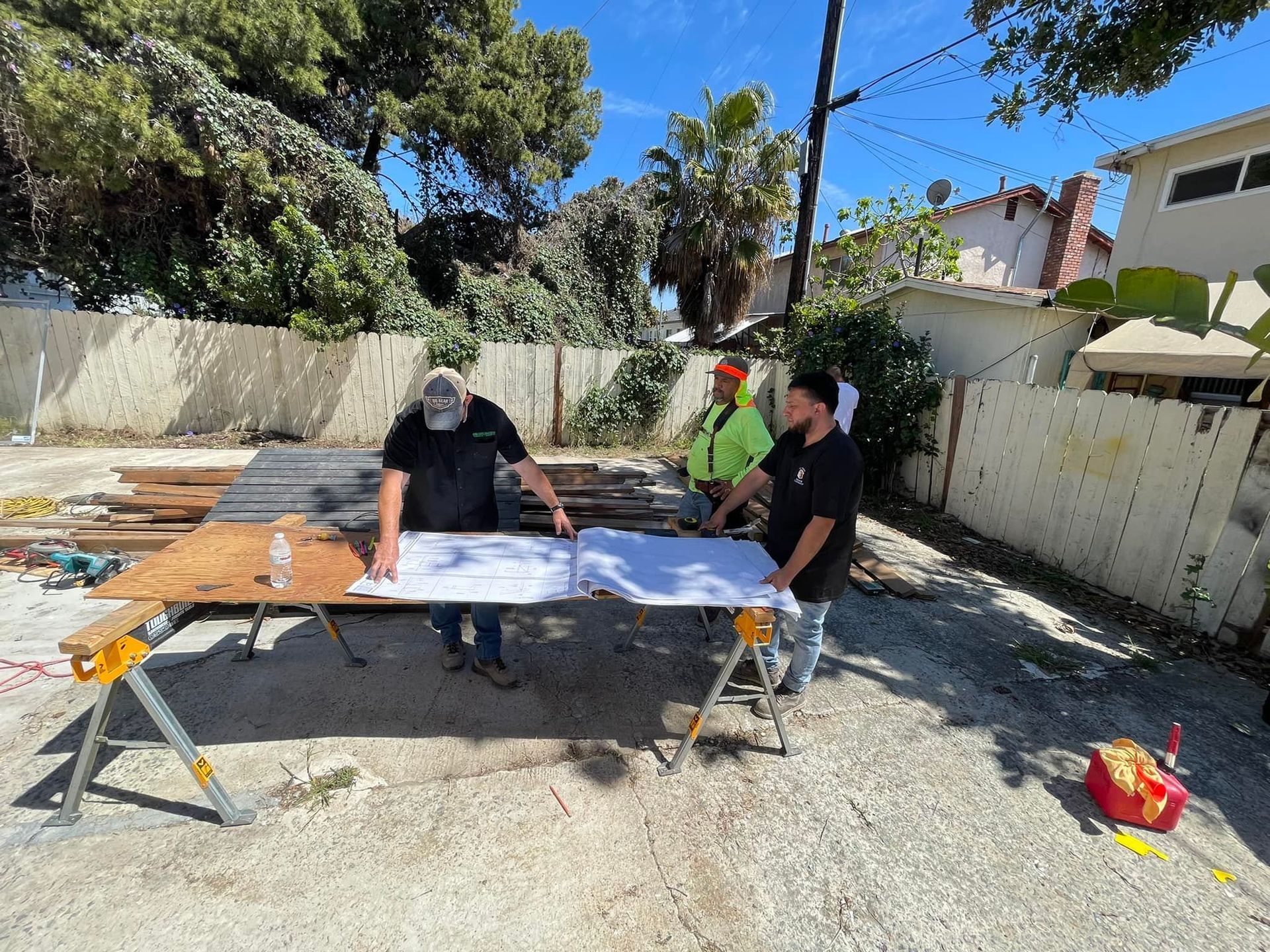 Three construction workers reviewing blueprints on a makeshift table outdoors.
