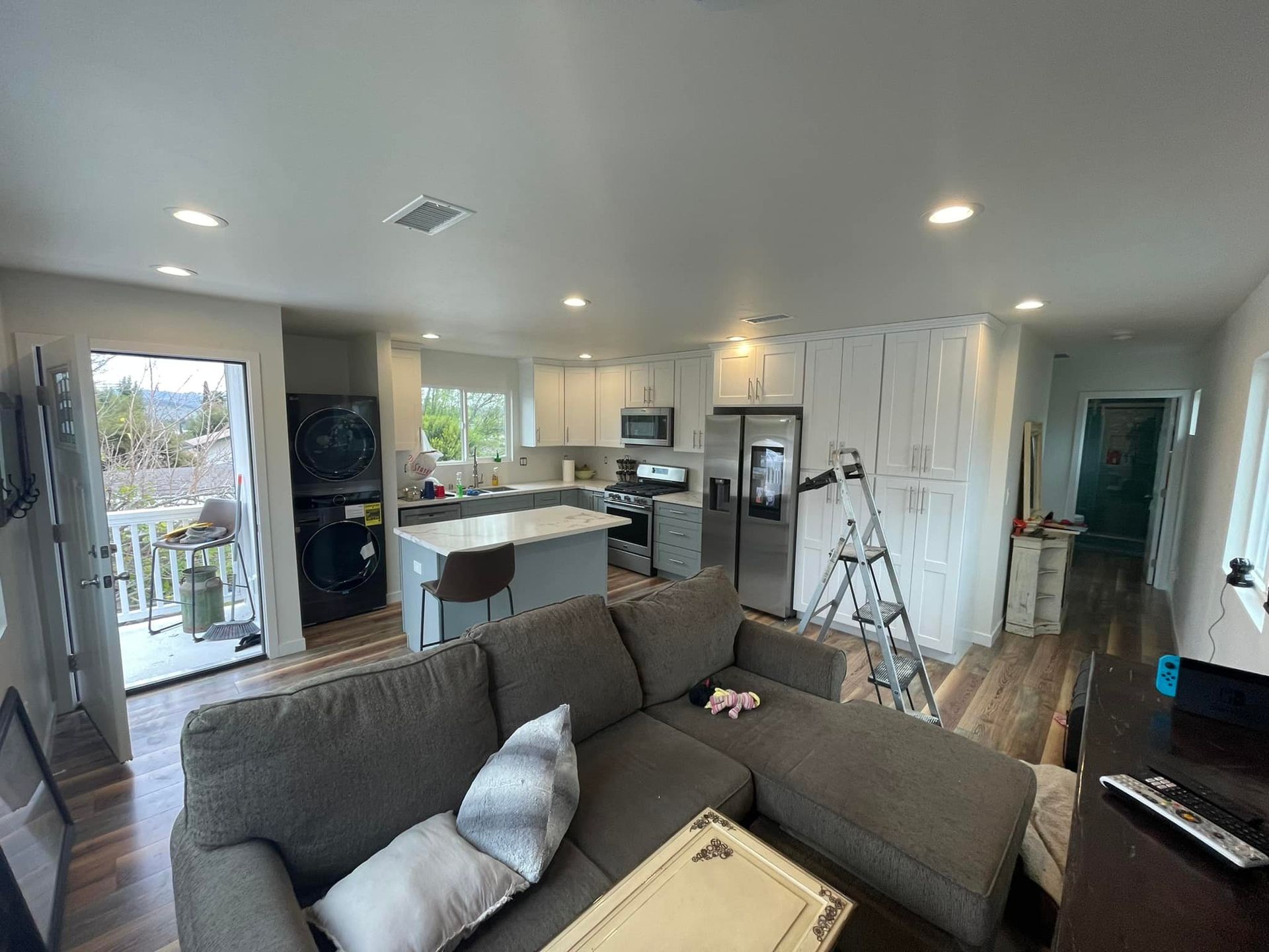 Open-concept kitchen and living room with gray cabinets, stainless steel appliances, and a gray sectional sofa.