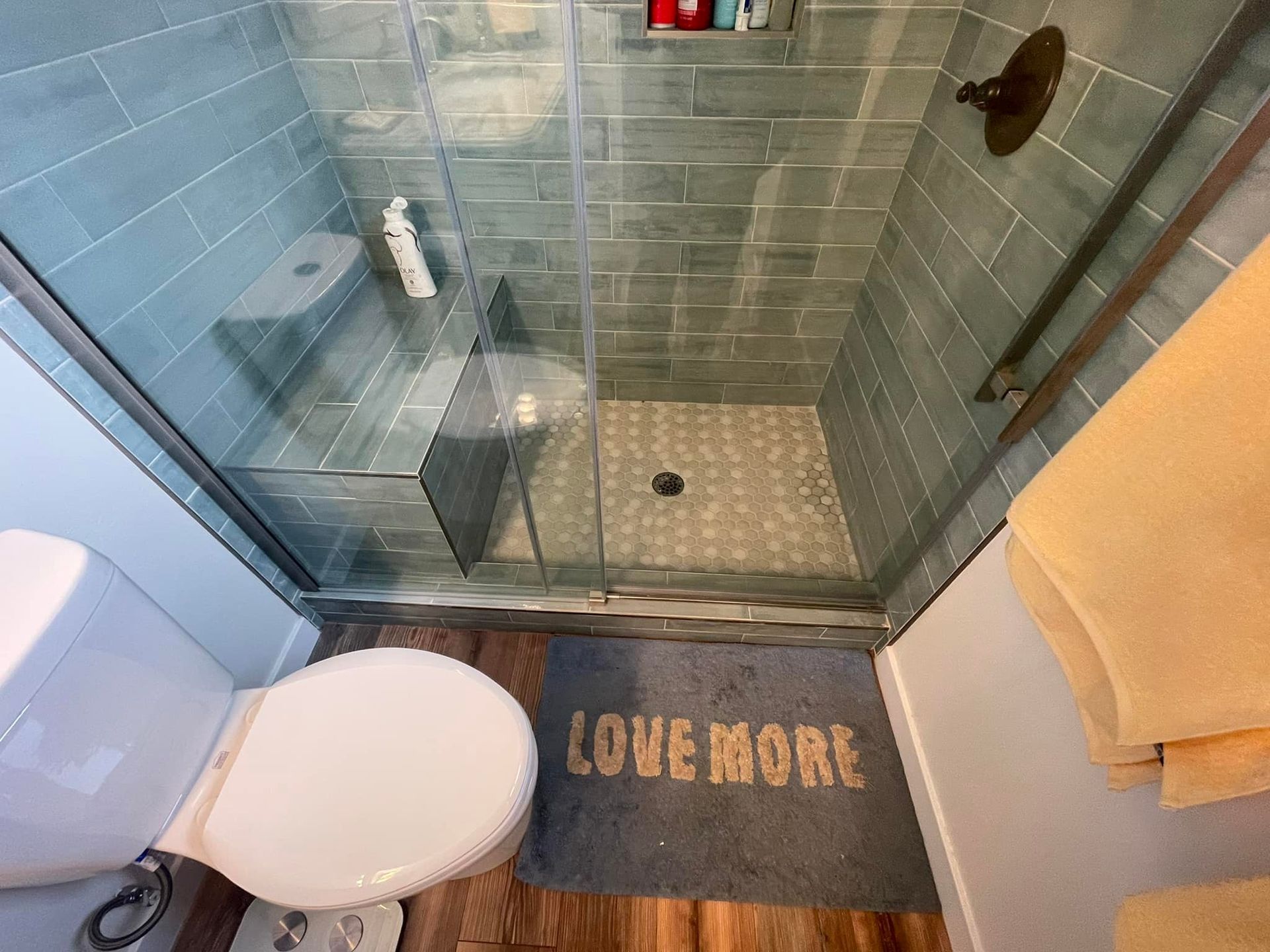 Bathroom with blue-tiled shower, glass doors, and a toilet. A 