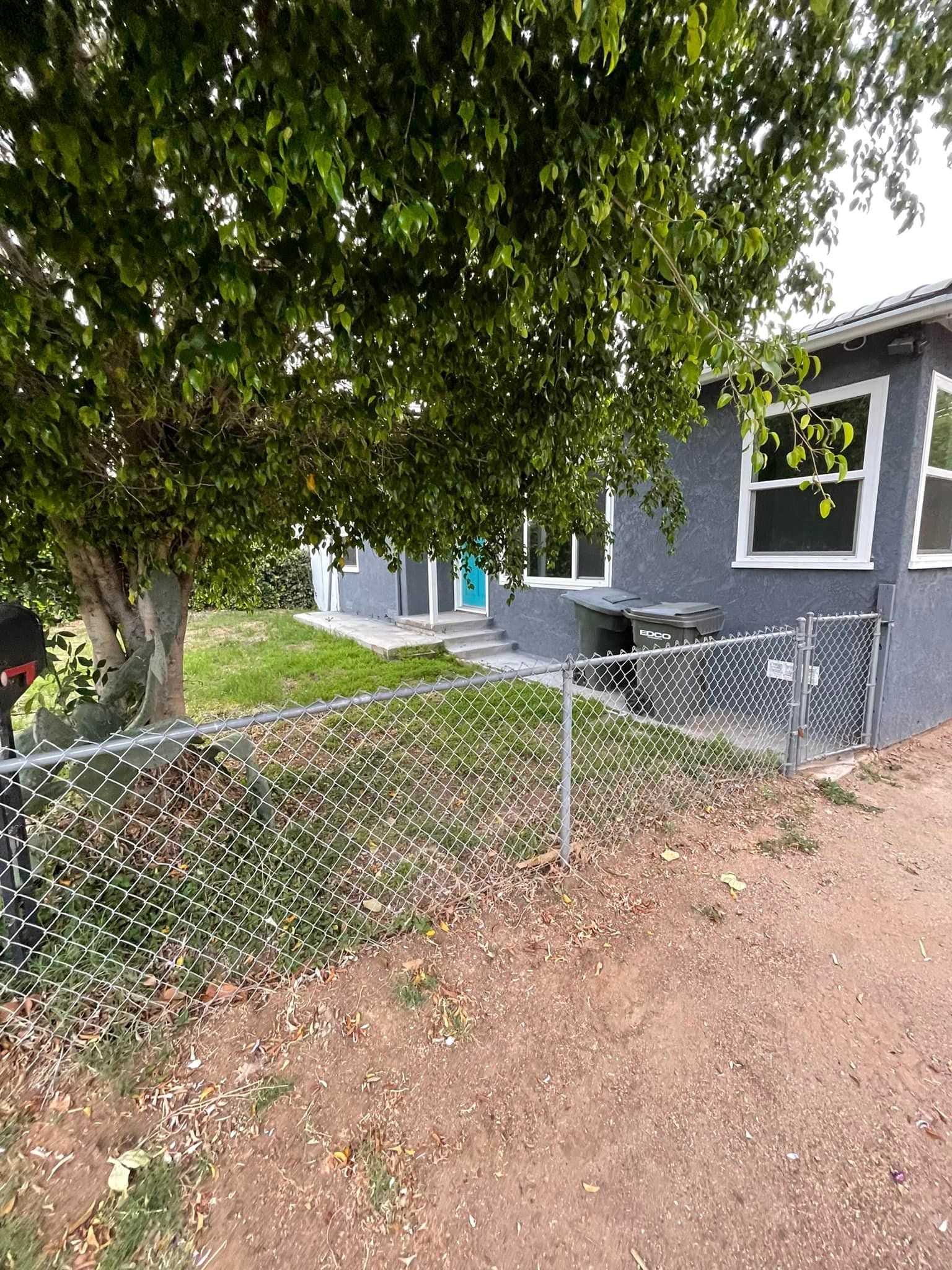 A house with a chain-link fence, tree, and gray exterior.