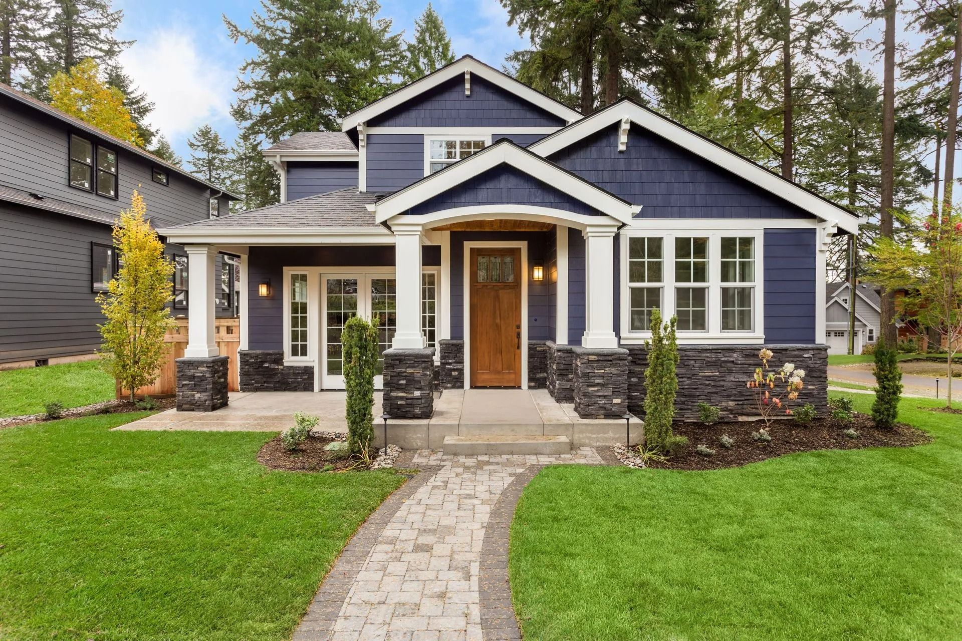 Blue house with white trim, brown door, stone accents, and paved walkway leading to the entrance.