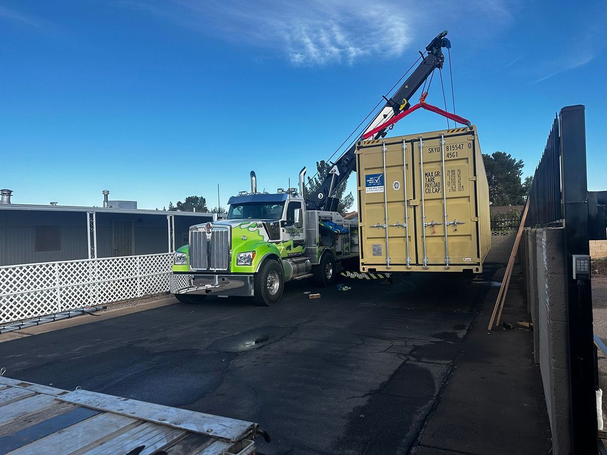 A semi-truck is carrying a shipping container with a crane attached to it.
